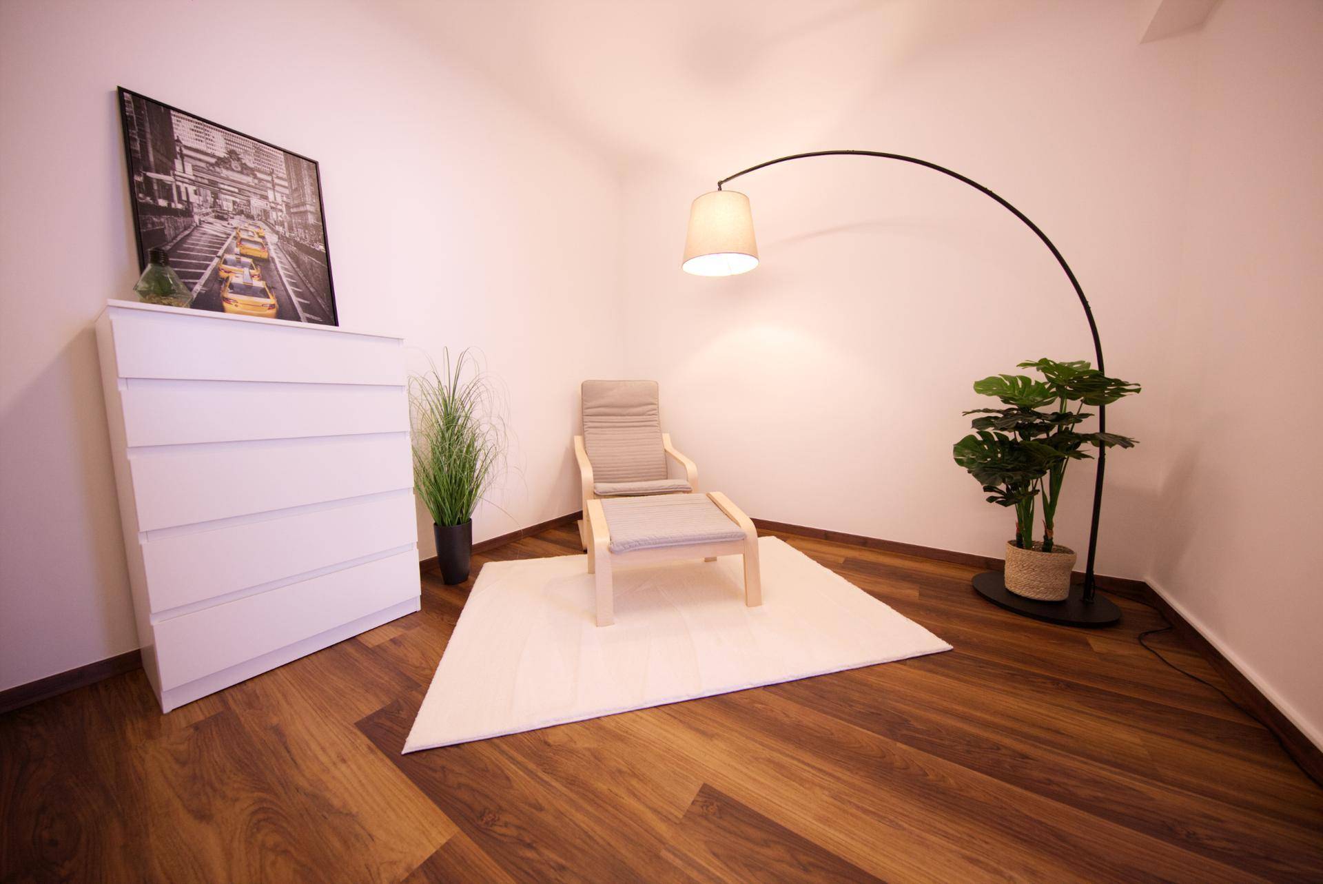 Gemütlicher Sessel mit Stehlampe und Pflanzen im hellen Zimmer, lädt zum Entspannen ein.