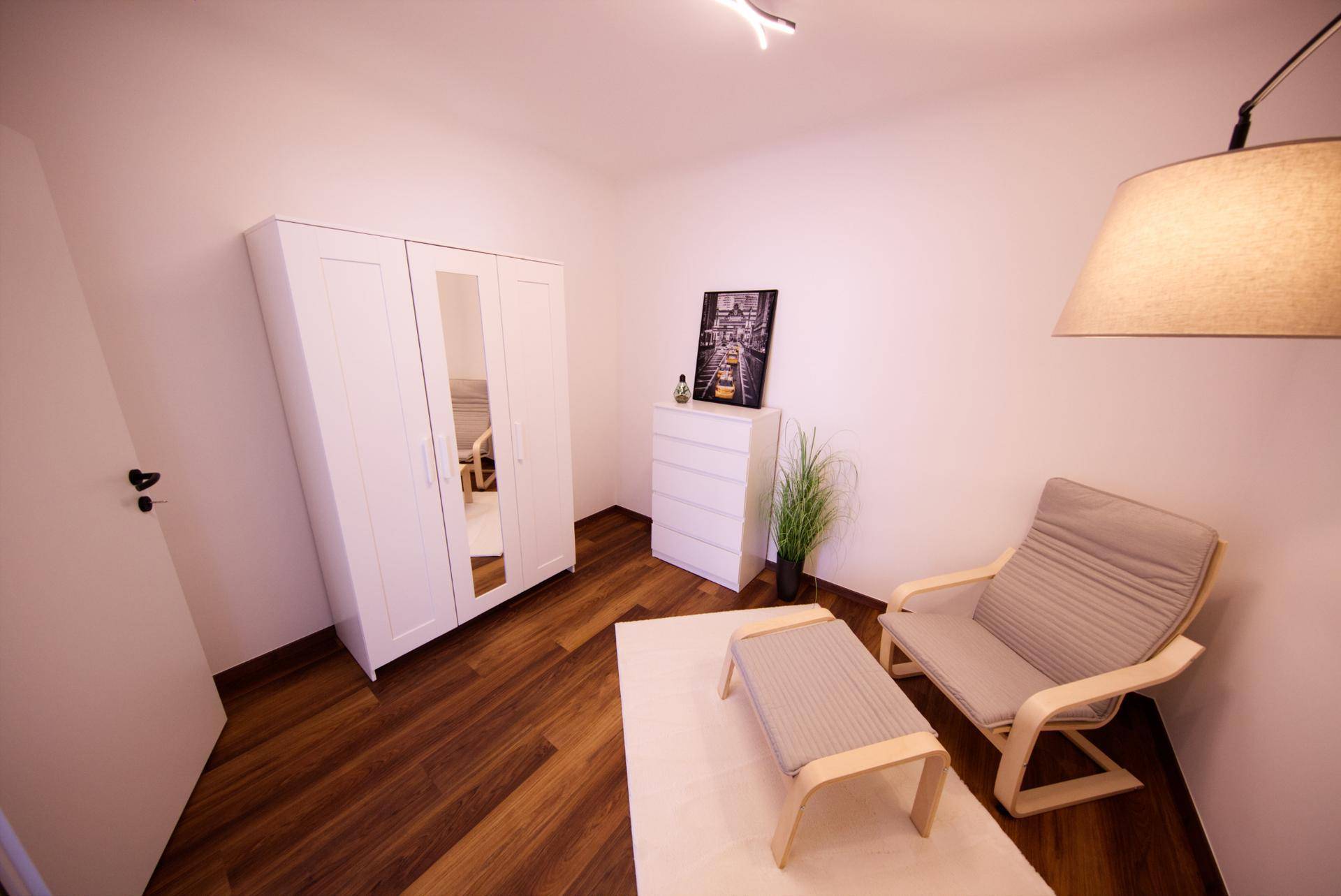 Zimmer mit weißem Kleiderschrank, Sessel und Holzboden, ideal als Gäste- oder Arbeitszimmer.