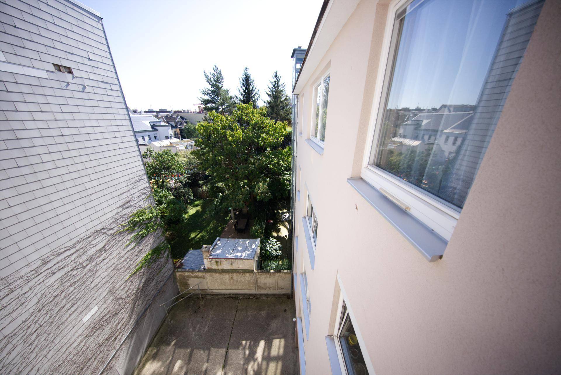 Außenbereich mit Betonfläche und Blick auf Bäume und Nachbargebäude, bietet Privatsphäre.