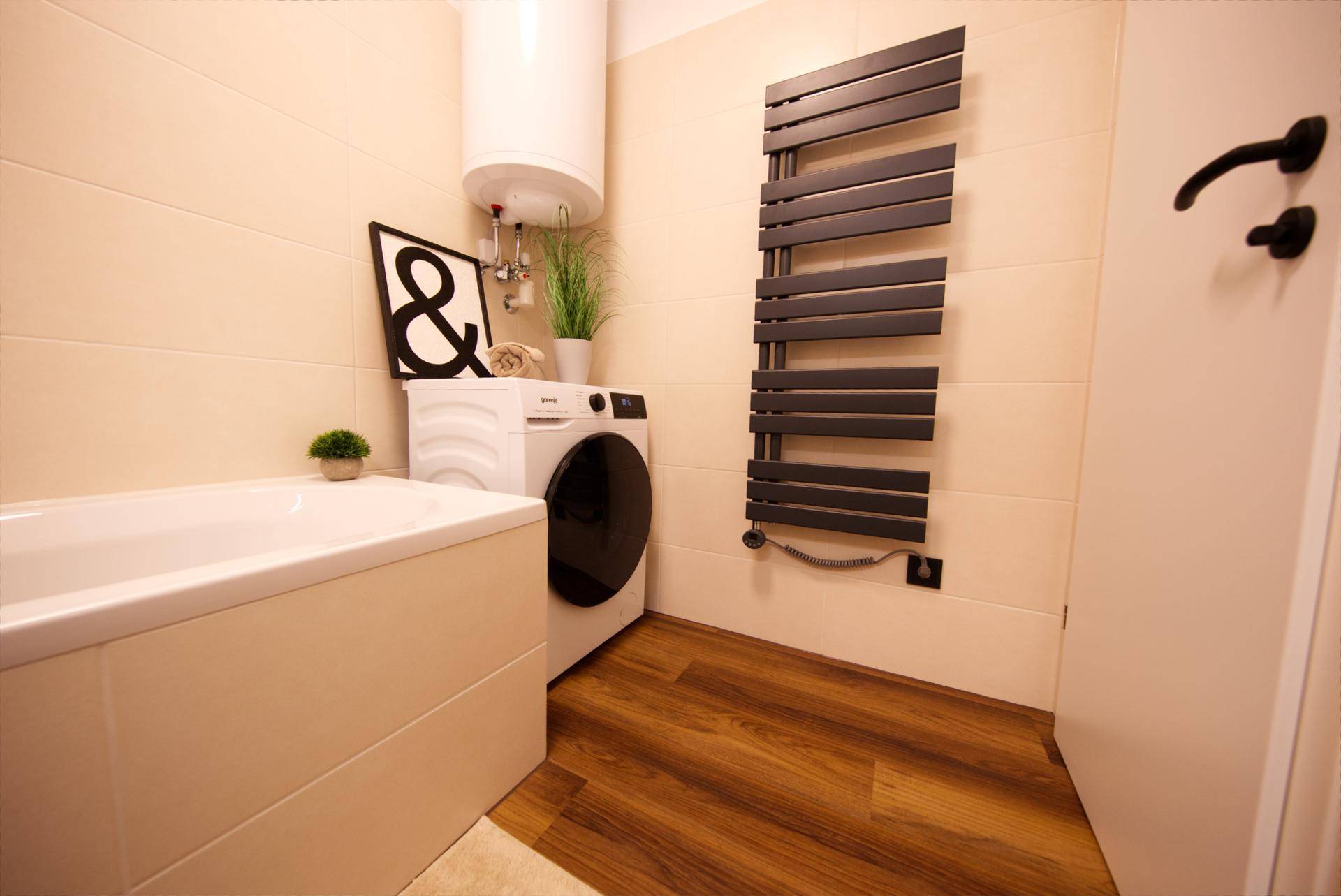 Badezimmer mit Badewanne, Waschmaschine und beheiztem Handtuchhalter, in hellen Farbtönen gehalten.