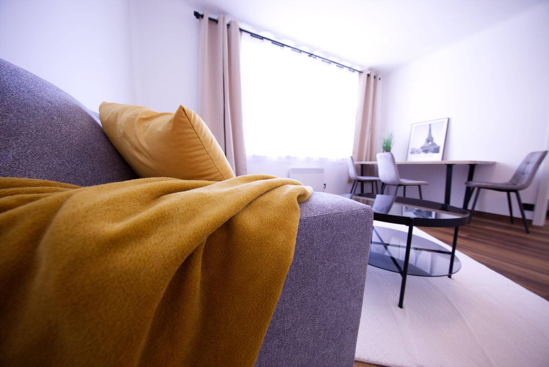 Gemütliches Sofa mit gelber Decke im hellen Wohnzimmer, mit Blick auf den Essbereich.