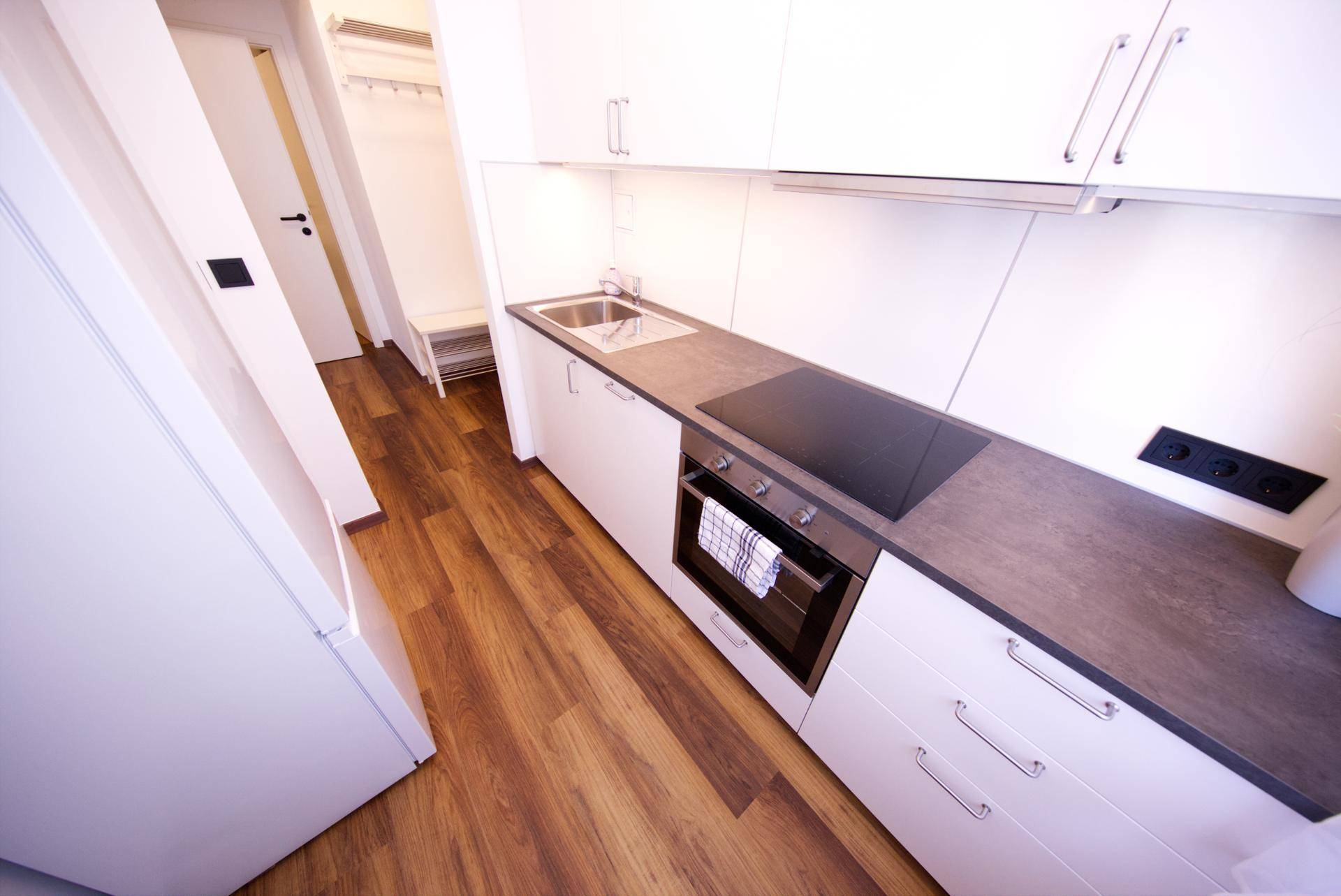 Schmale Küche mit weißen Schränken, Spüle und Kochfeld, mit Holzboden und modernem Design.