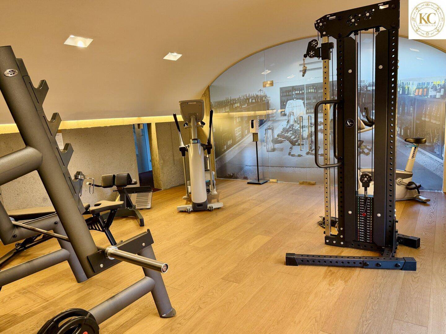 Gut ausgestatteter Fitnessraum mit verschiedenen Trainingsgeräten und Holzboden.