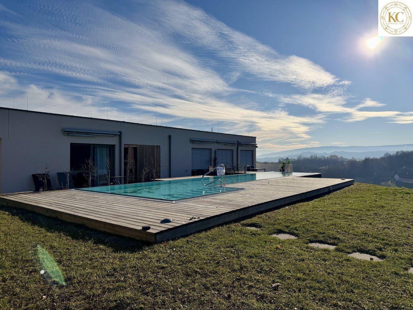 Außenansicht des Gebäudes mit Infinity-Pool, umgeben von einer Holzterrasse und grüner Landschaft.