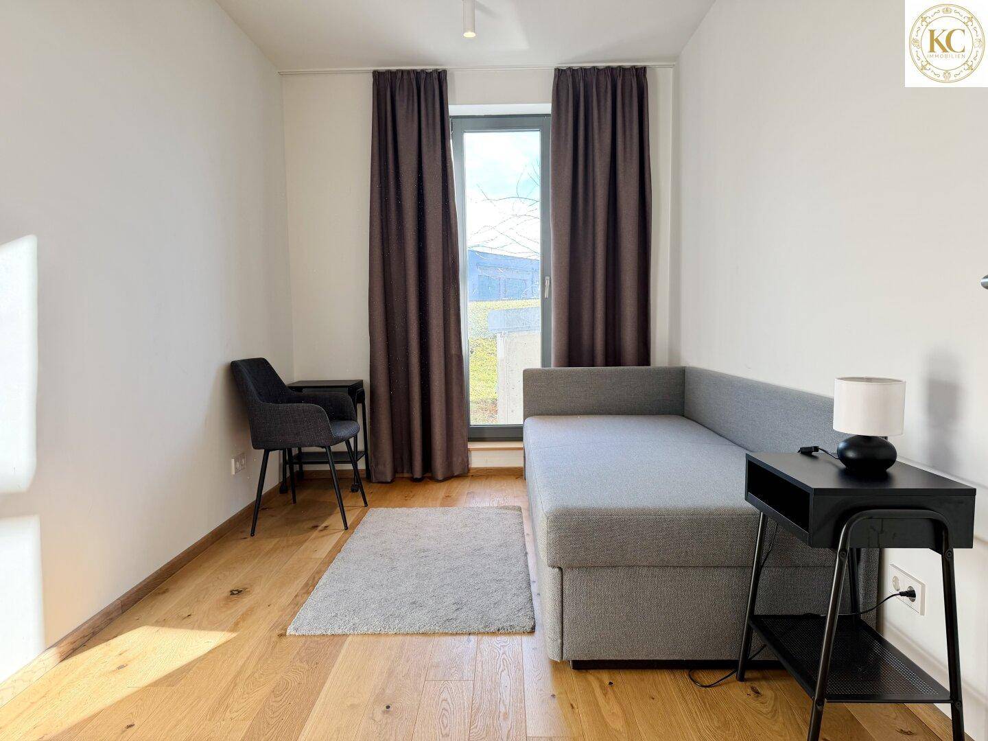Helles Gästezimmer mit Schlafsofa, Holzboden und großem Fenster für viel Tageslicht.