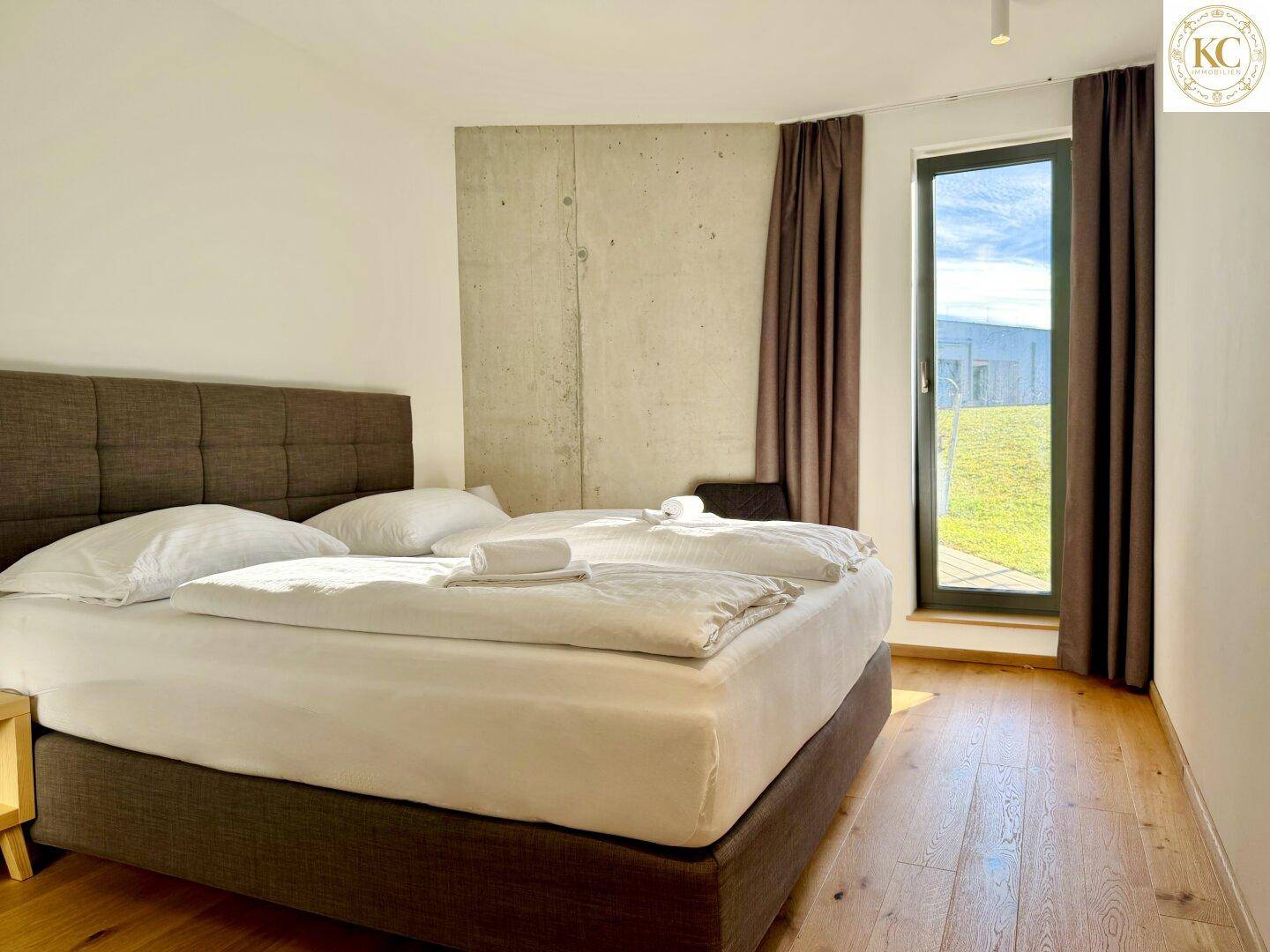 Gemütliches Schlafzimmer mit Doppelbett, Holzboden und Fenster mit Blick ins Grüne.