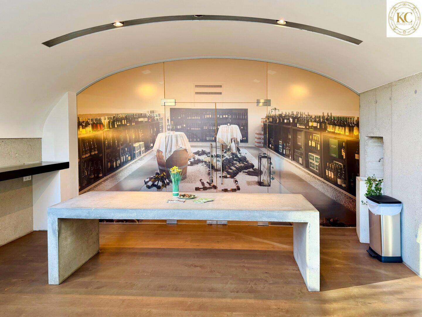 Großer Raum mit modernem Betontisch und einer Wandmalerei, die einen Weinkeller darstellt.