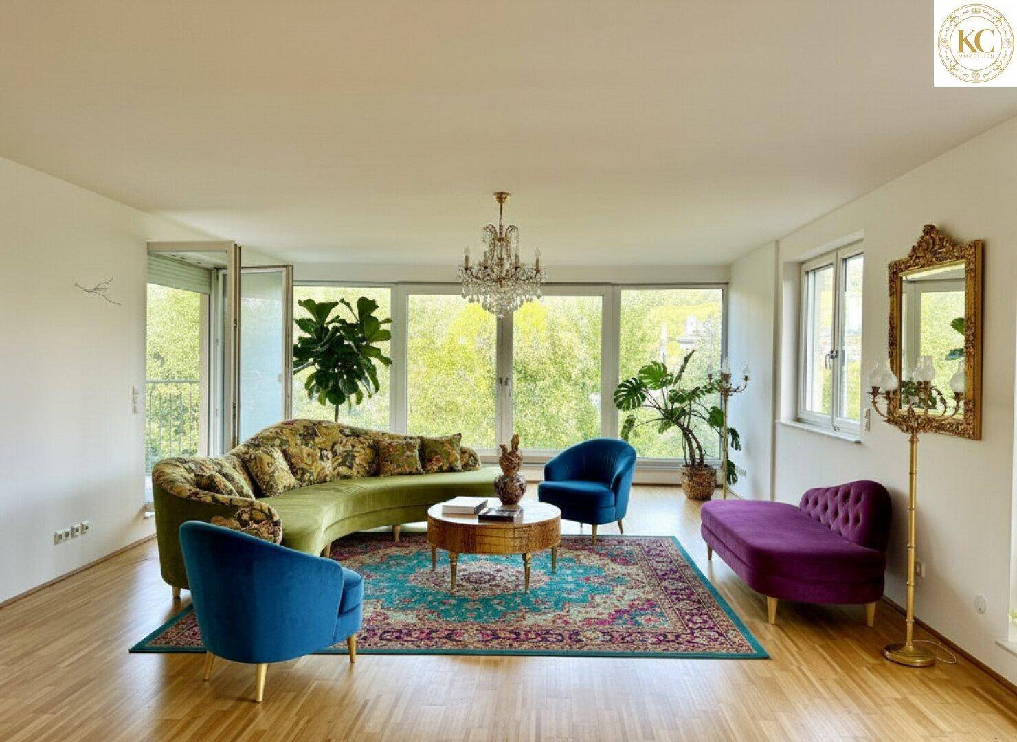 Farbenfrohes Wohnzimmer mit eleganten Möbeln, Kronleuchter und großen Fenstern mit Blick ins Grüne.