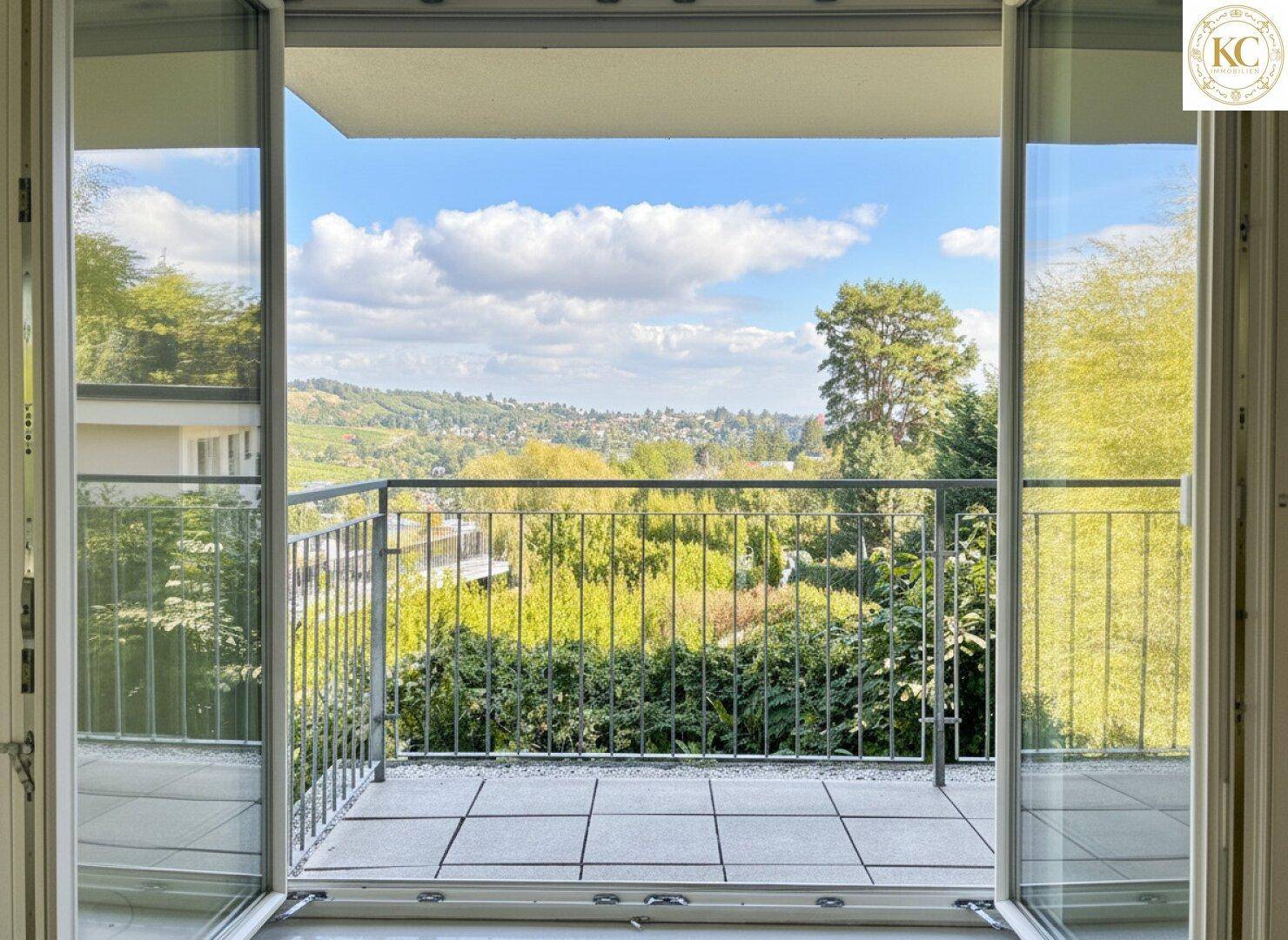 Balkon mit Metallgeländer und weitem Blick über die grüne Landschaft und umliegende Bebauung.