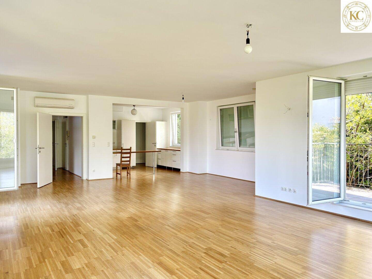Geräumiger Wohnbereich mit Parkettboden und Zugang zu einer offenen Küchenzeile, ideal für Essbereich.