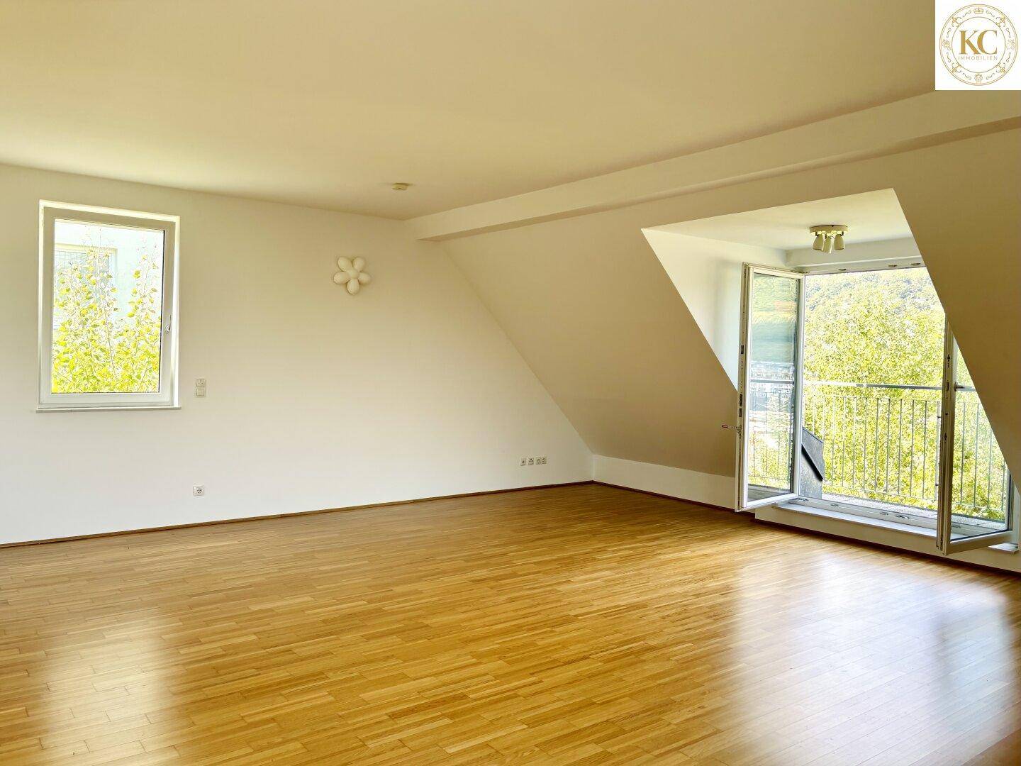 Helles, leeres Schlafzimmer im Dachgeschoss mit Holzboden und Zugang zu einem kleinen Balkon.