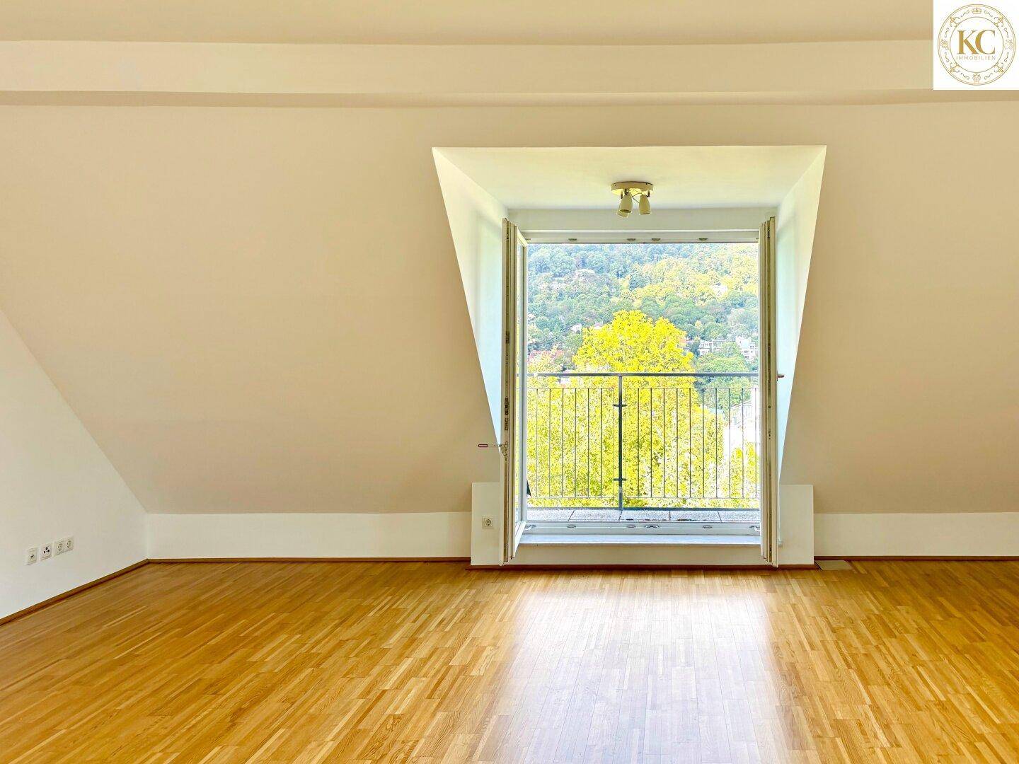 Leerer Raum im Dachgeschoss mit Holzboden und direktem Zugang zu einem kleinen Balkon mit Aussicht.
