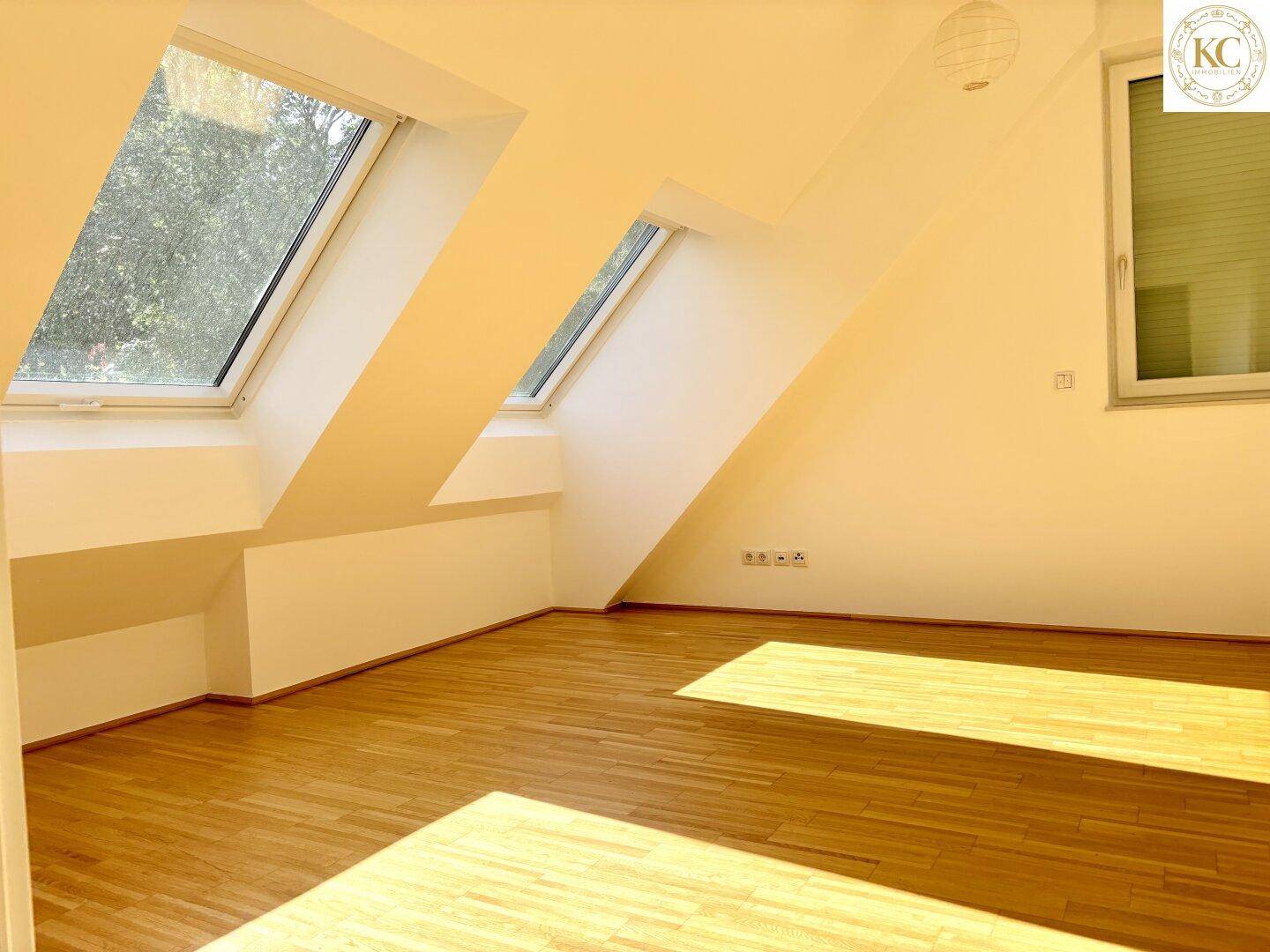 Leerer Raum im Dachgeschoss mit Holzboden, schrägen Wänden und großen Dachfenstern für viel Licht.