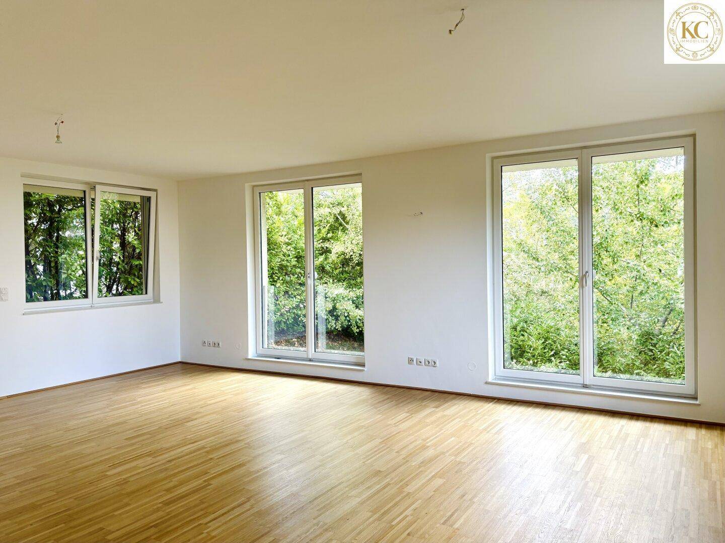 Leerer Raum mit Holzboden und großen Fenstern, die einen schönen Blick ins Grüne bieten.