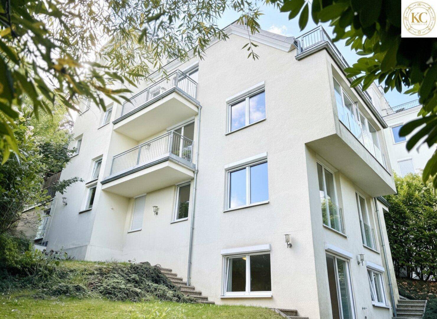 Moderne Wohnhausfassade mit mehreren Balkonen und großen Fenstern, eingebettet in grüne Umgebung.