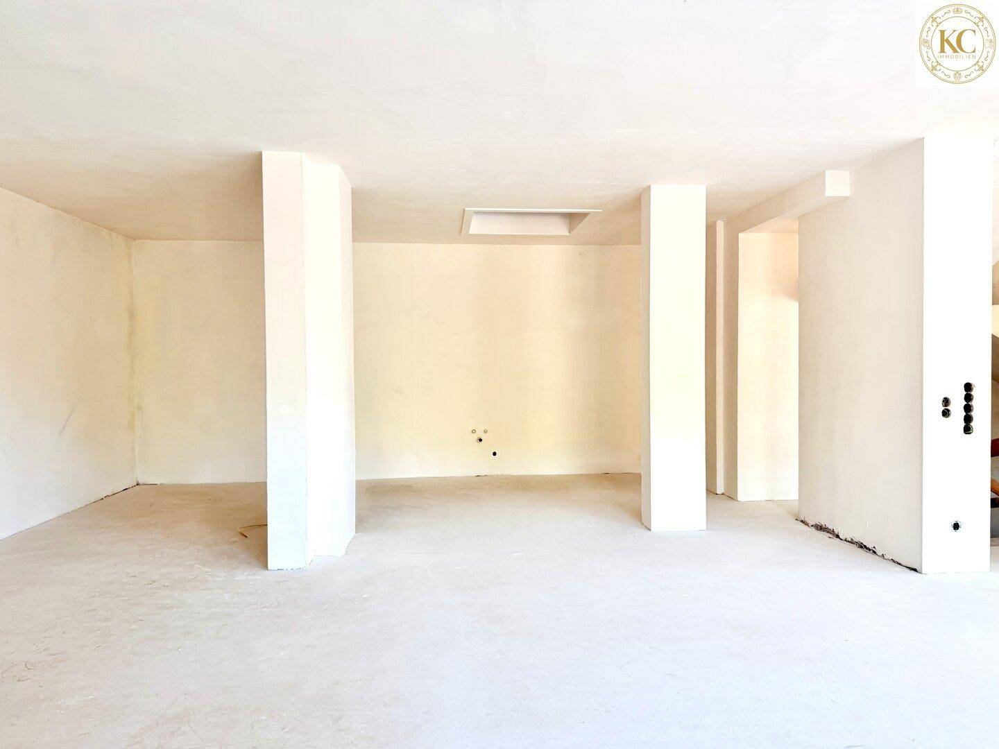 Leerer Raum im Rohbau mit tragenden Säulen und unfertigen Wänden, bereit für den Ausbau.