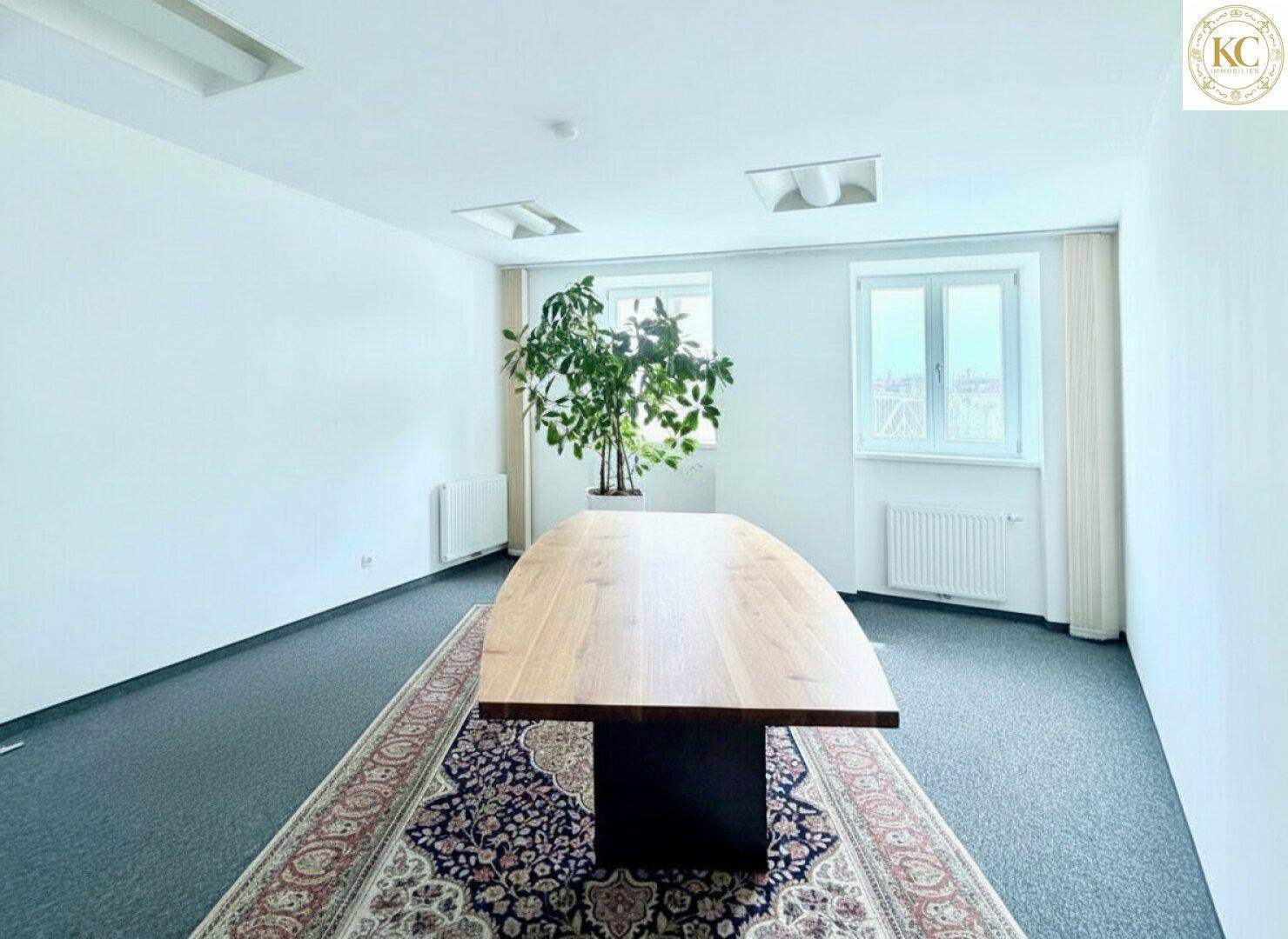 Konferenzraum mit großem Holztisch, Teppichboden und einem dekorativen Teppich in der Mitte.