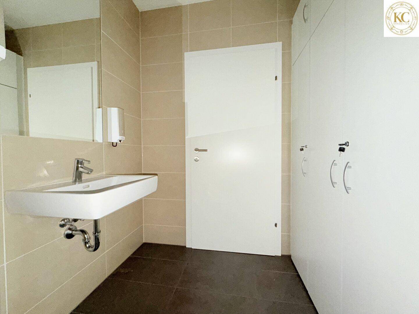 Sanitärbereich mit Waschbecken, Fliesenboden und weißen Spinden für persönliche Gegenstände.