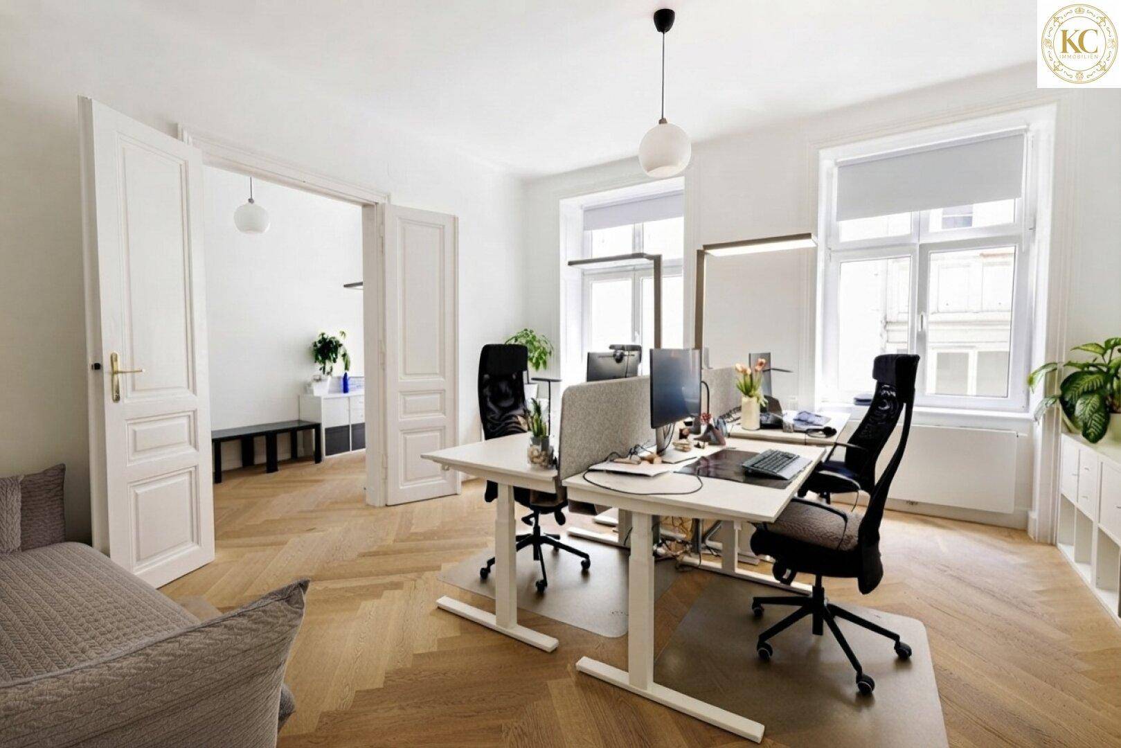 Helles Büro mit mehreren Arbeitsplätzen, bequemer Couch und Fischgrätparkettboden.