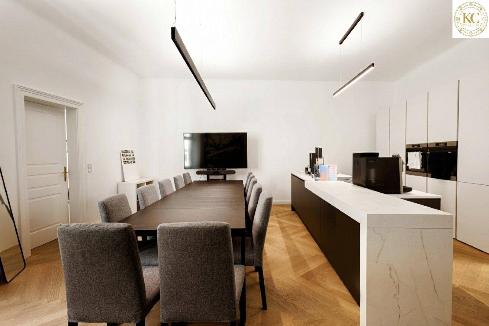 Moderner offener Bereich mit langer Tafel, integrierter Küche und minimalistischer Beleuchtung.
