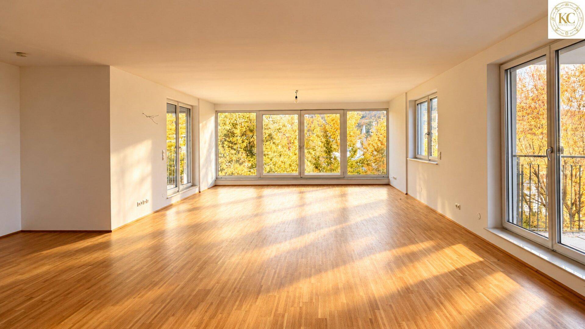 Helles, leeres Wohnzimmer mit großen Fenstern, Parkettboden und Blick auf herbstliche Bäume.