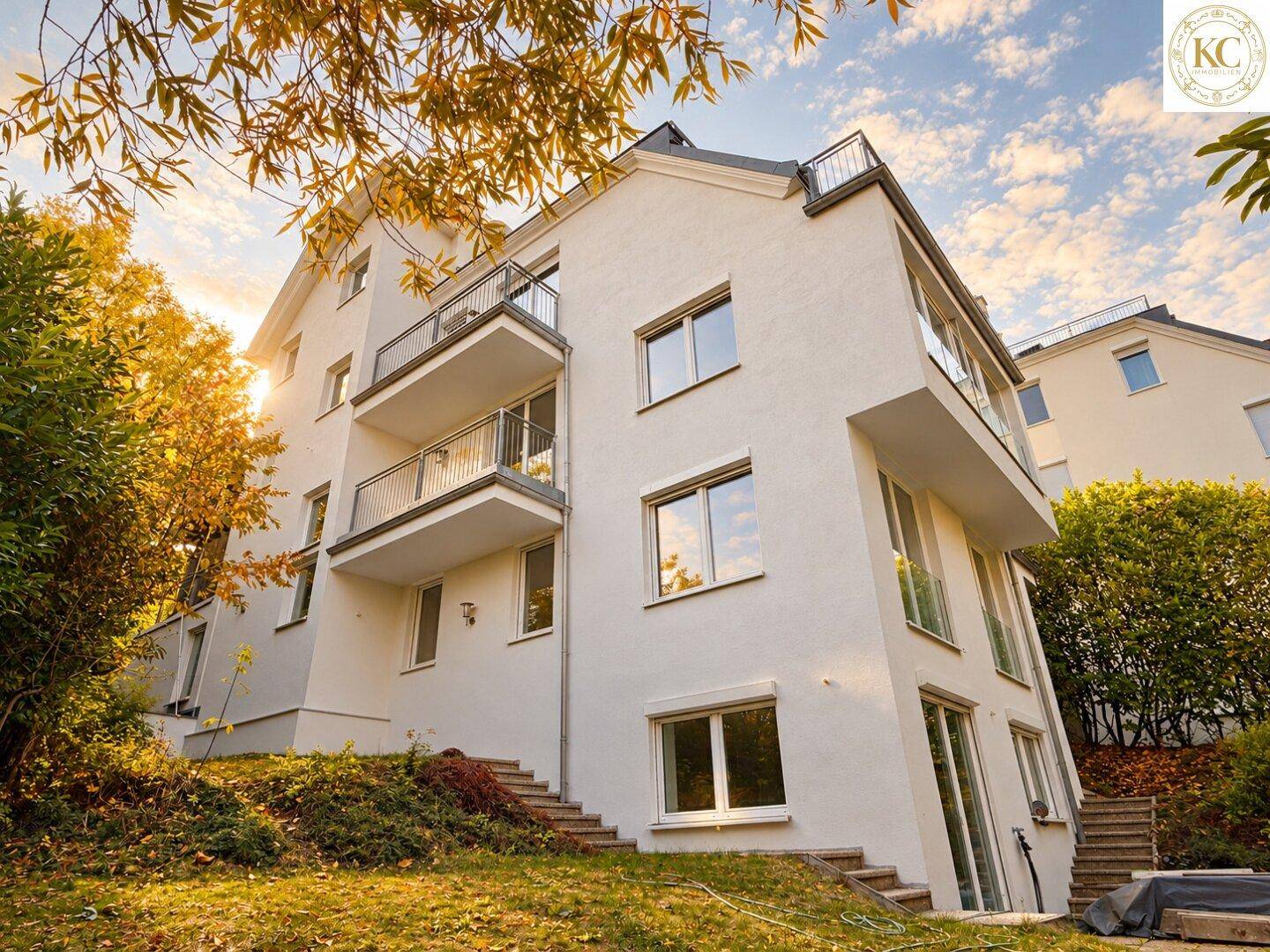 Modernes Mehrfamilienhaus mit weißer Fassade, Balkonen und großen Fenstern in grüner Umgebung.