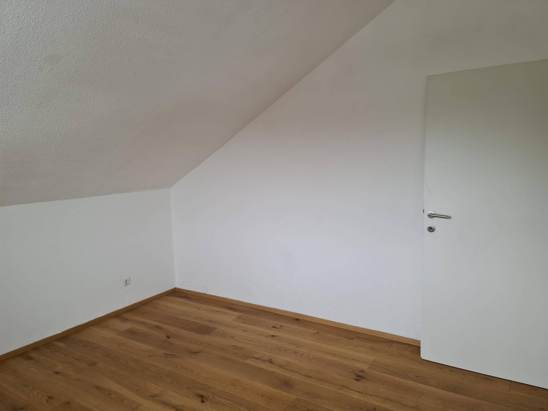 Kleines Zimmer im Dachgeschoss mit Holzboden und schräger Decke.