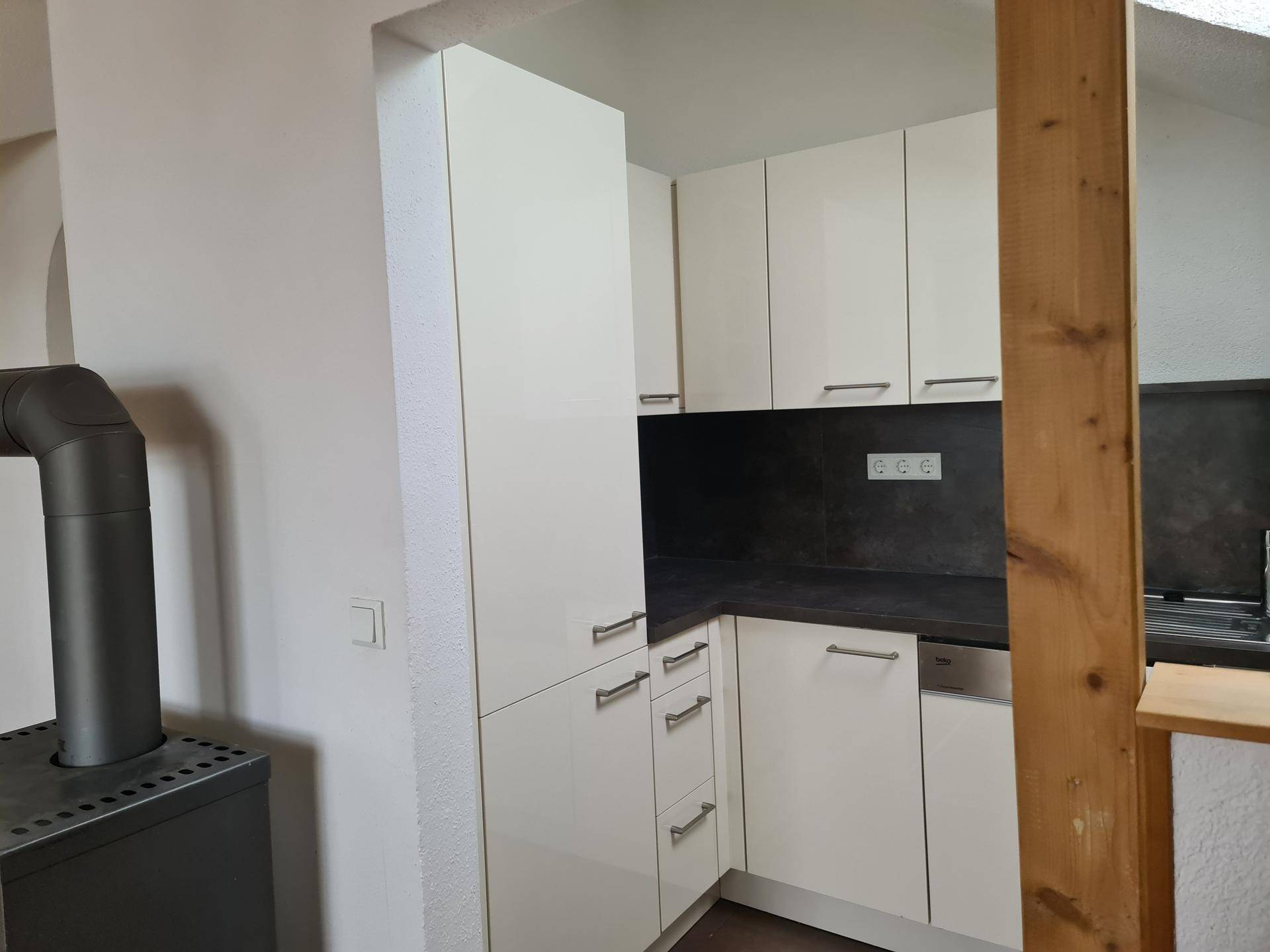 Weiße Einbauküche mit glänzenden Fronten und integrierten Geräten im Dachgeschoss.