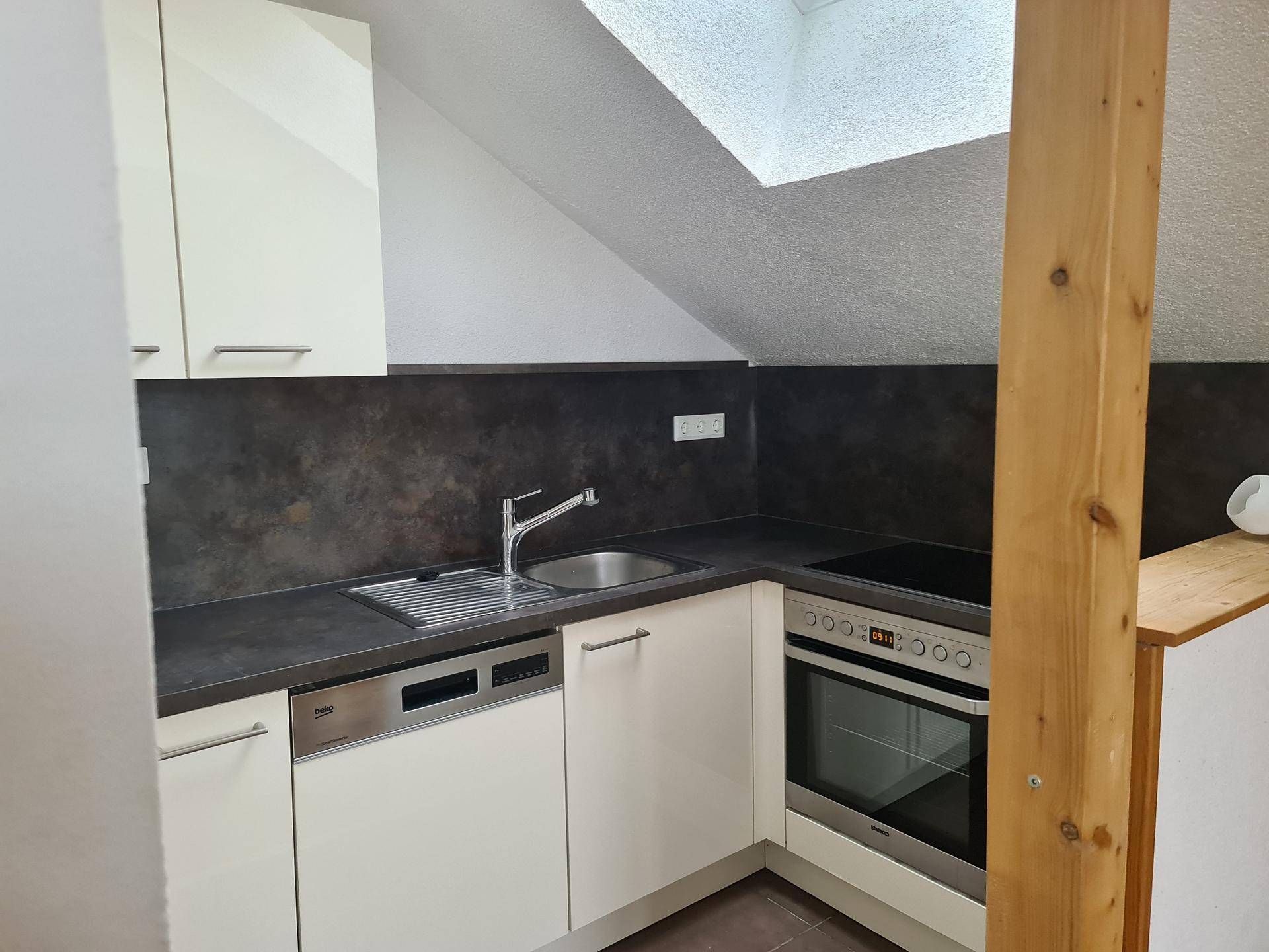 Funktionale Küche mit Spüle, Kochfeld und Backofen unter einem Dachfenster.