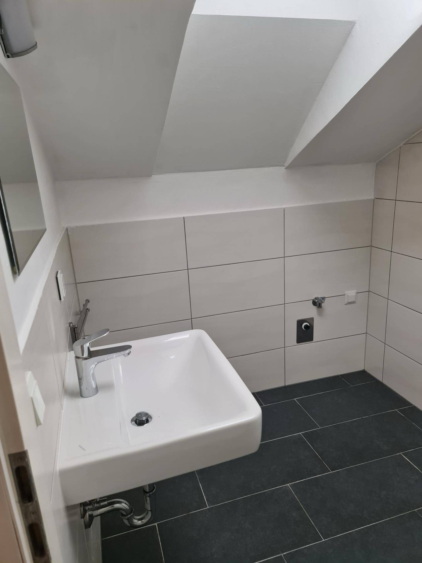 Modernes Badezimmer mit Waschbecken, hellen Fliesen und dunklem Boden.