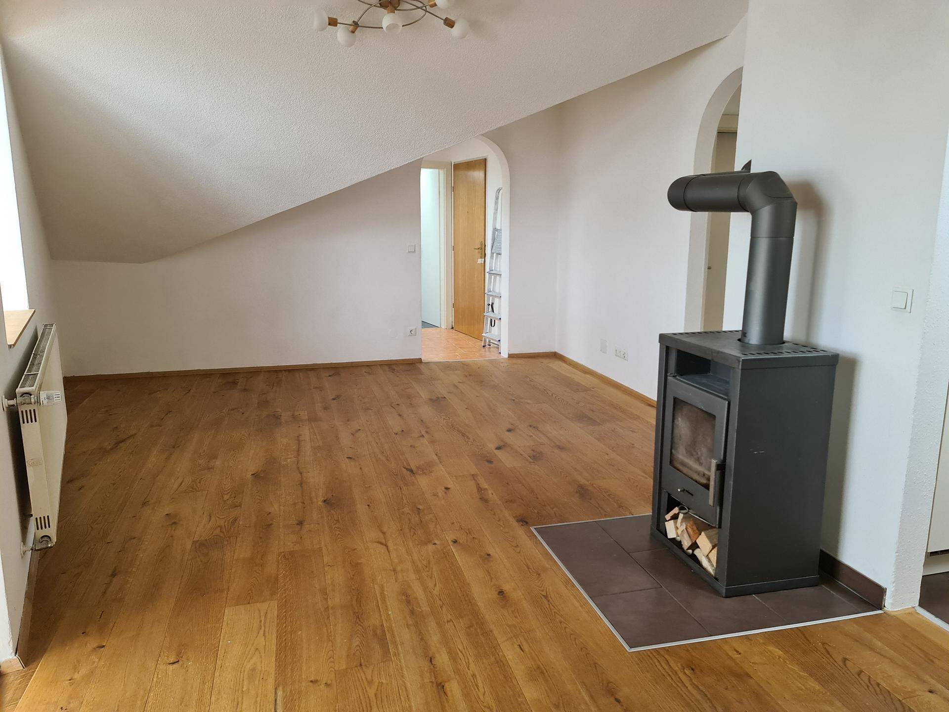 Helles Wohnzimmer im Dachgeschoss mit Holzboden und modernem Kaminofen.