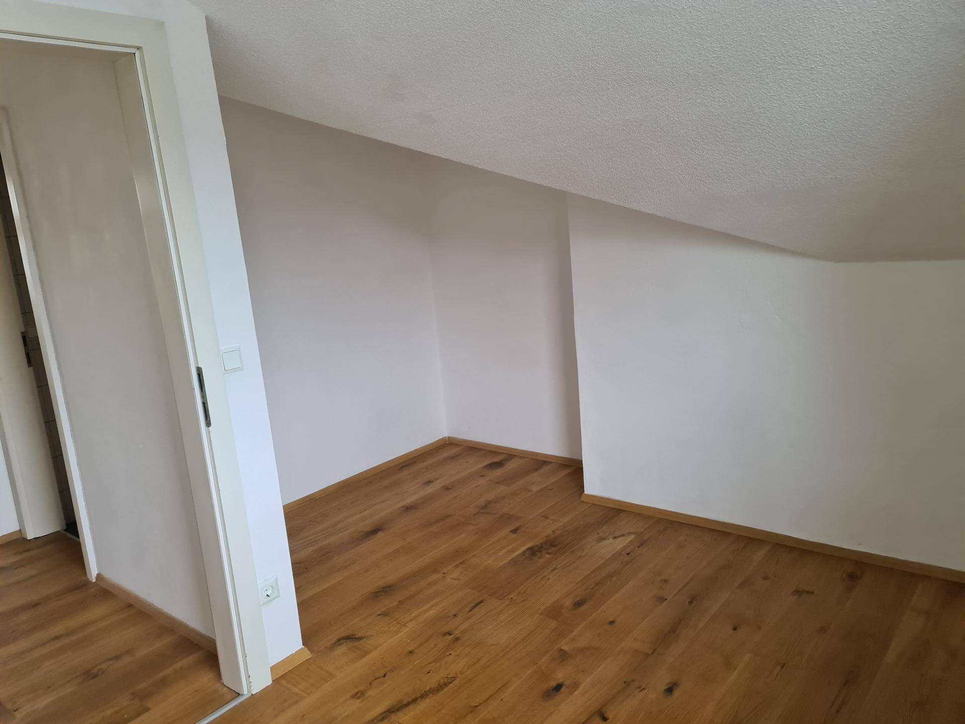 Helles Zimmer im Dachgeschoss mit Holzboden und schrägen Wänden.