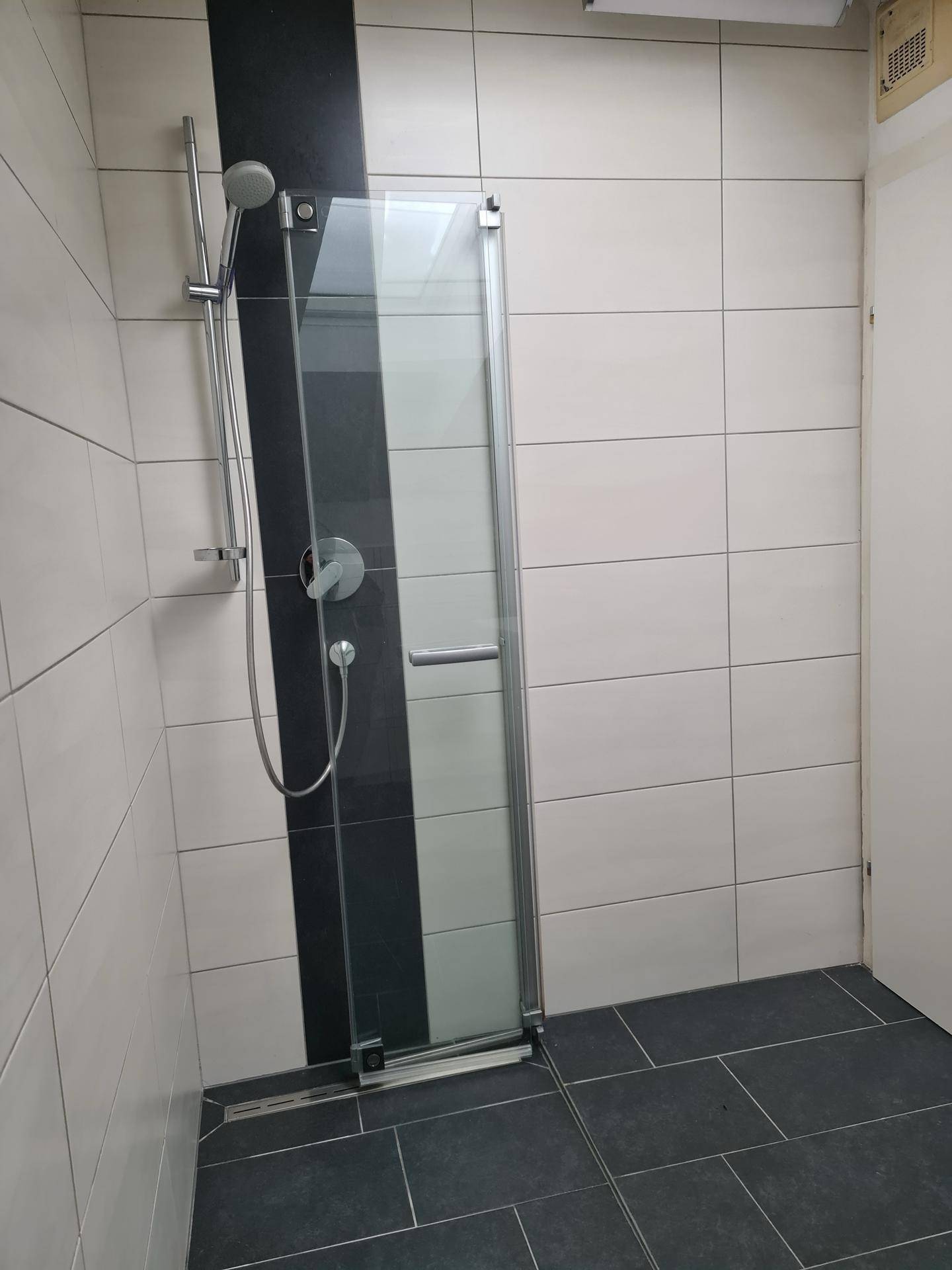 Modernes Badezimmer mit ebenerdiger Dusche, Glaswand und dunklen Bodenfliesen.