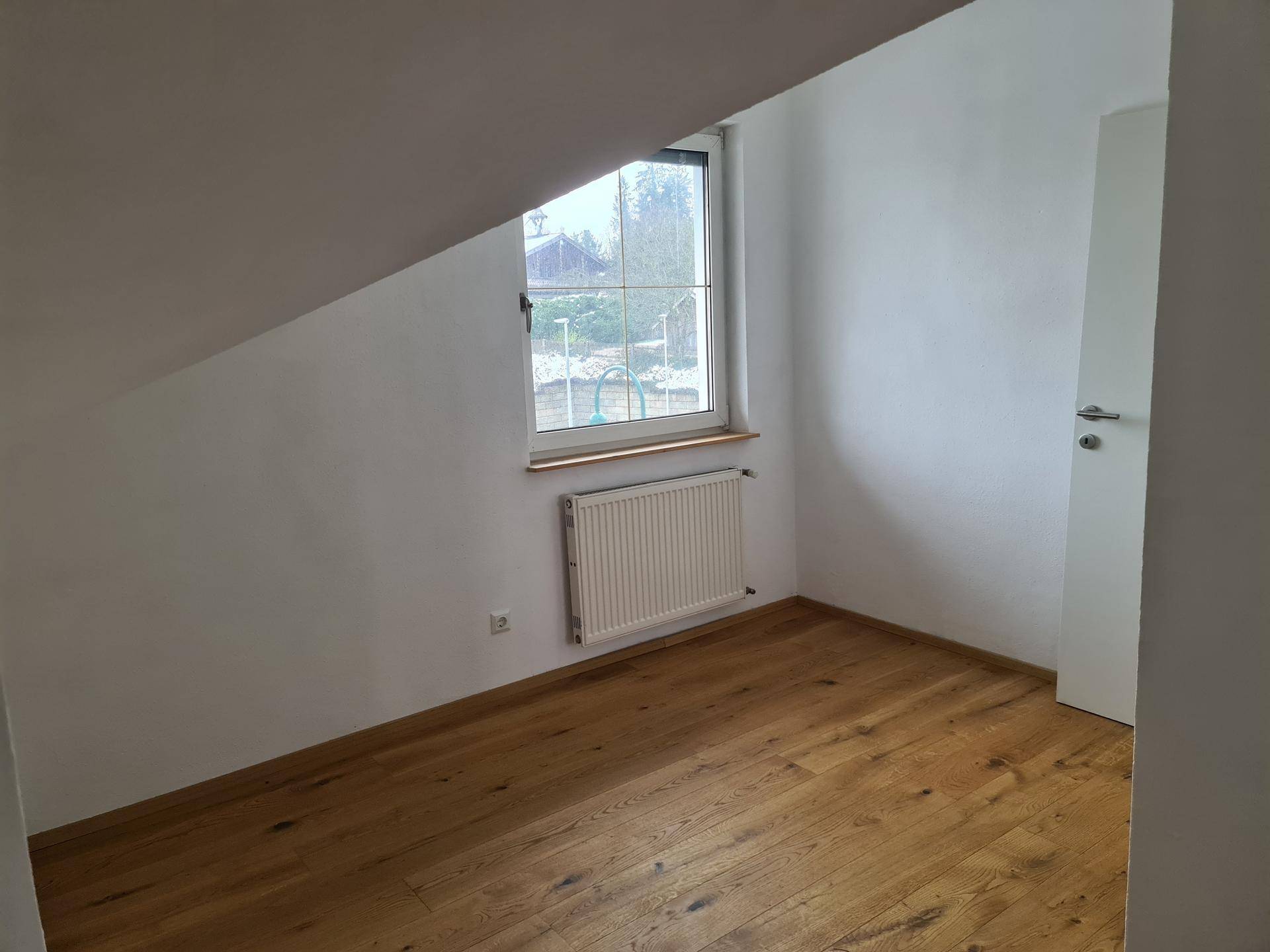 Gemütliches Zimmer im Dachgeschoss mit Holzboden, Fenster und Heizkörper.