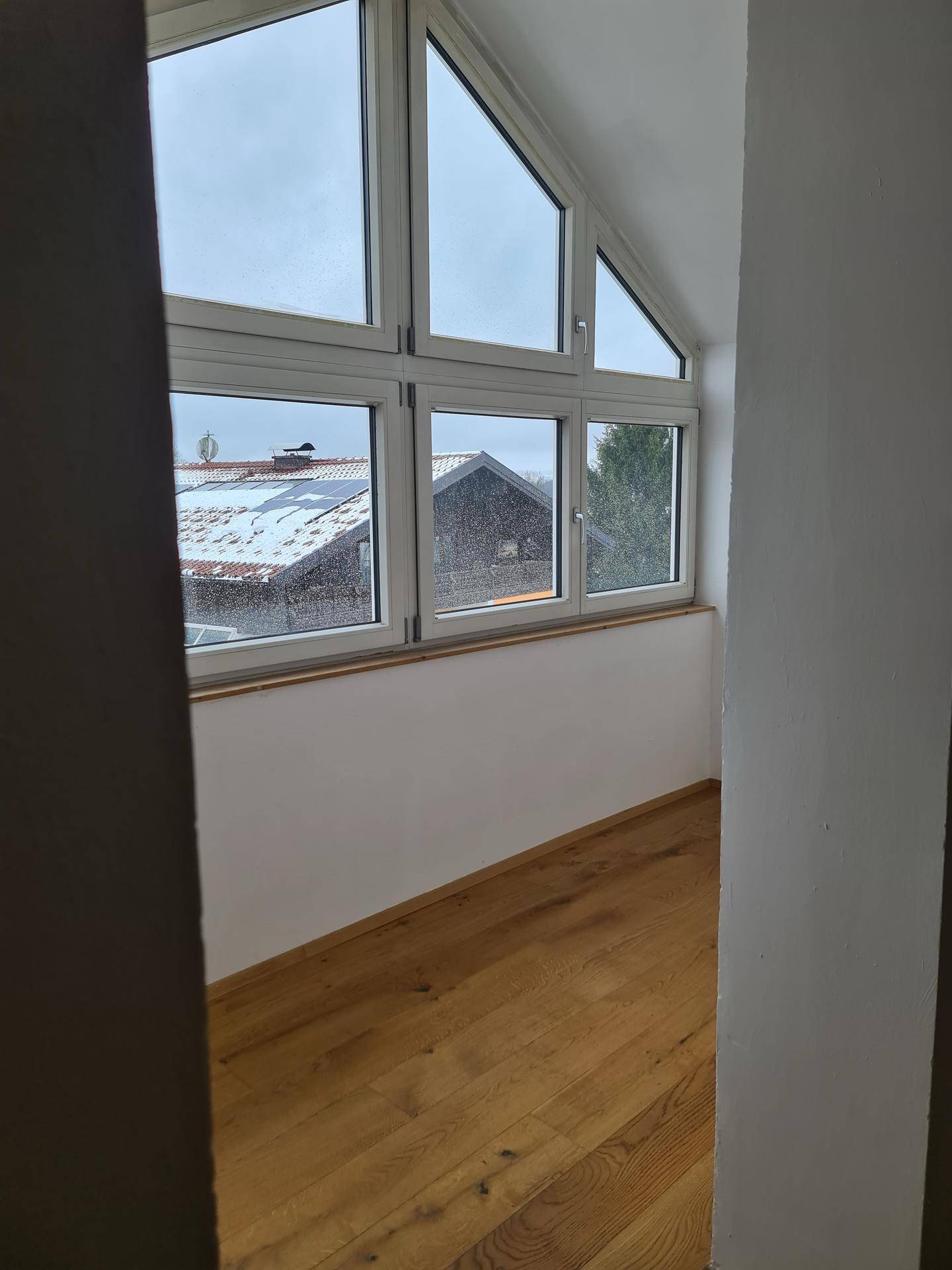 Helles Zimmer mit Holzboden und großen Fenstern, die einen Blick nach draußen bieten.