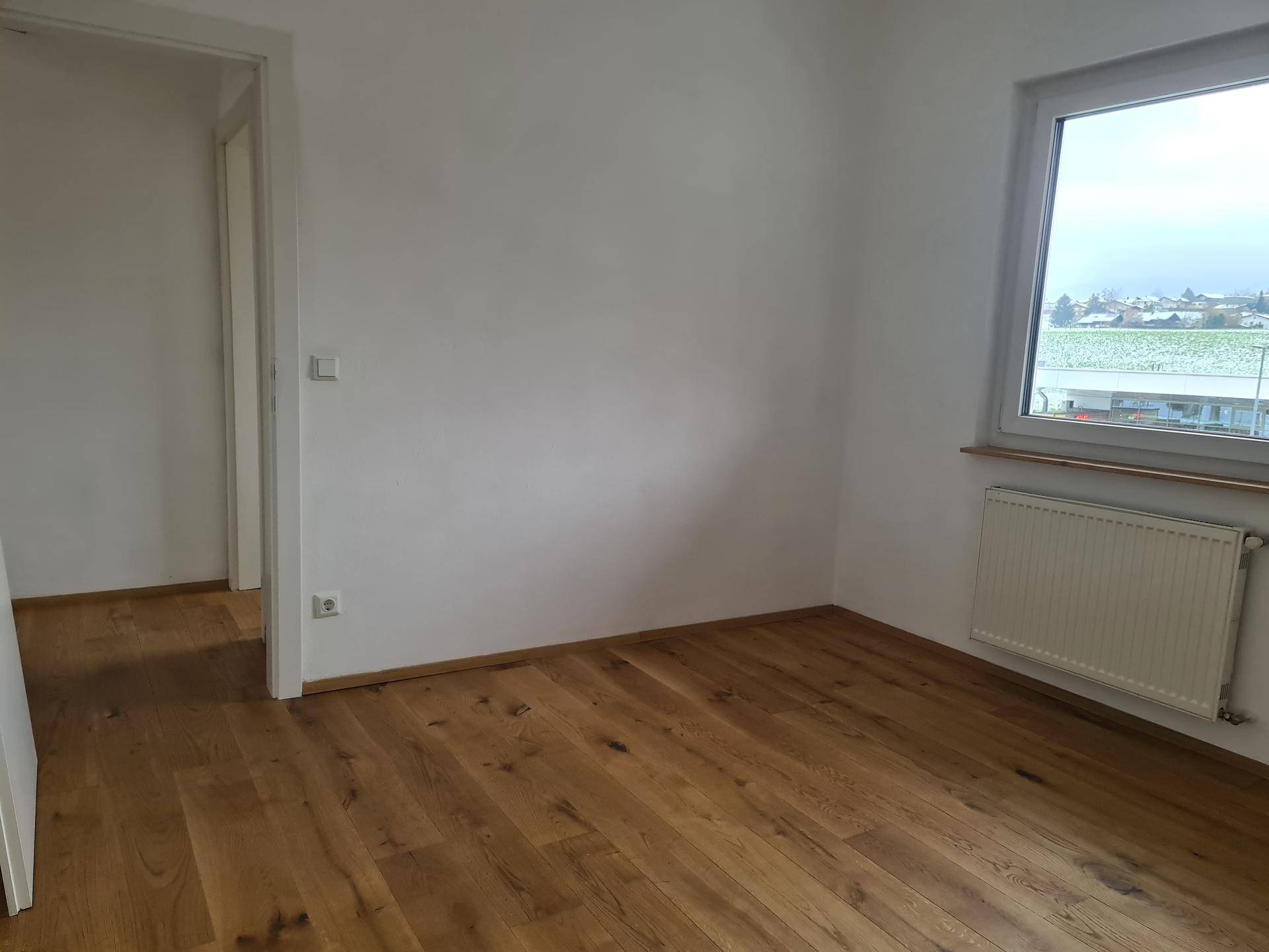 Geräumiges Zimmer mit Holzboden und Fenster, das viel Tageslicht hereinlässt.