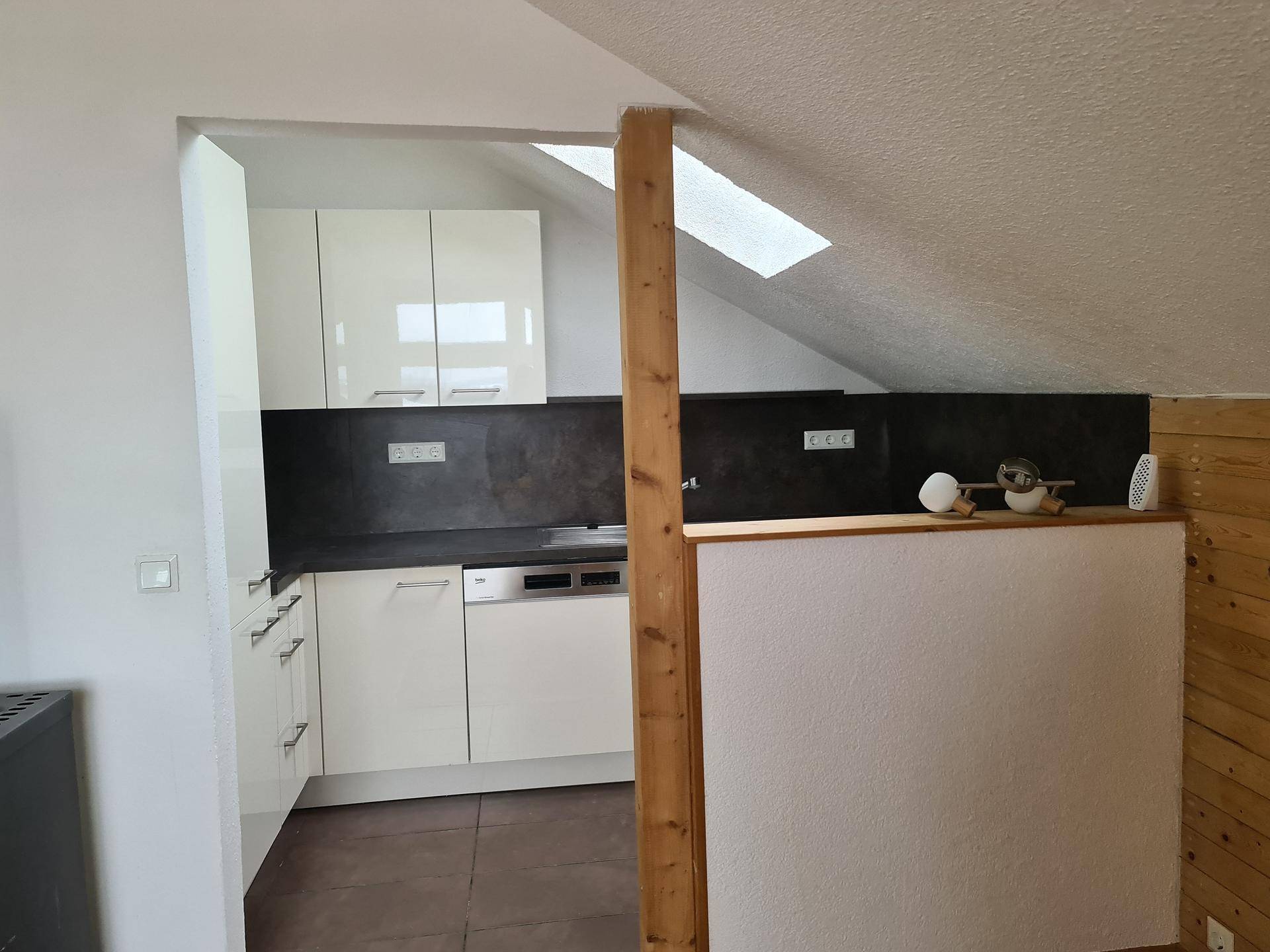 Moderne Einbauküche im Dachgeschoss mit weißen Schränken, dunkler Arbeitsplatte und Dachfenster.