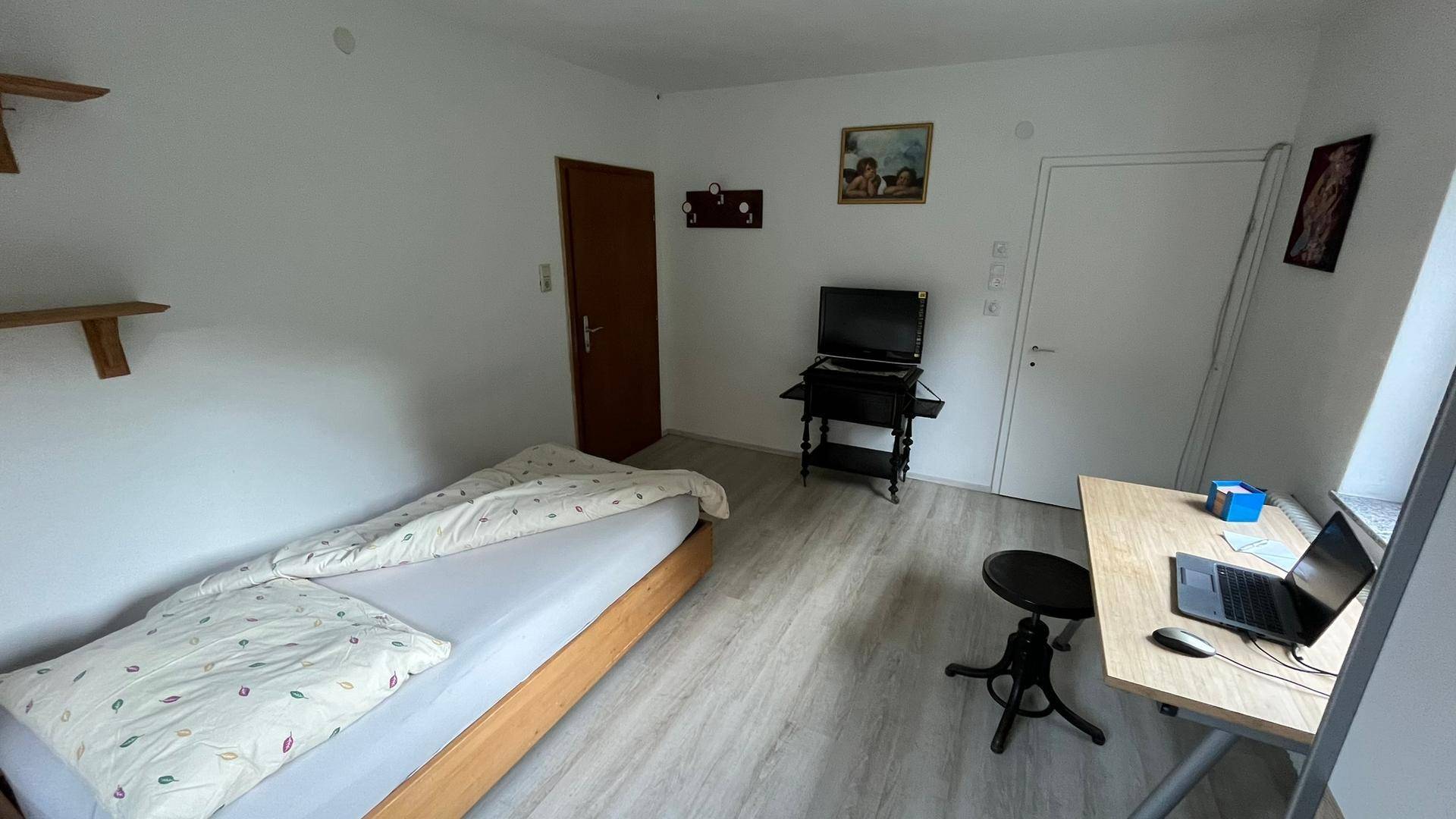 Gemütliches Schlafzimmer mit Einzelbett, Schreibtisch und hellem Laminatboden für eine Person.
