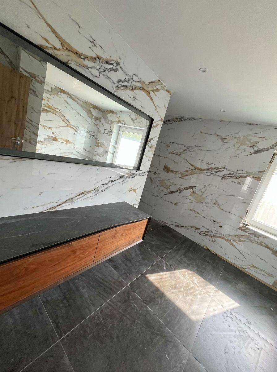 Geräumiges Badezimmer mit großem Spiegel, schwebendem Unterschrank und Marmor-Effekt-Wandfliesen.