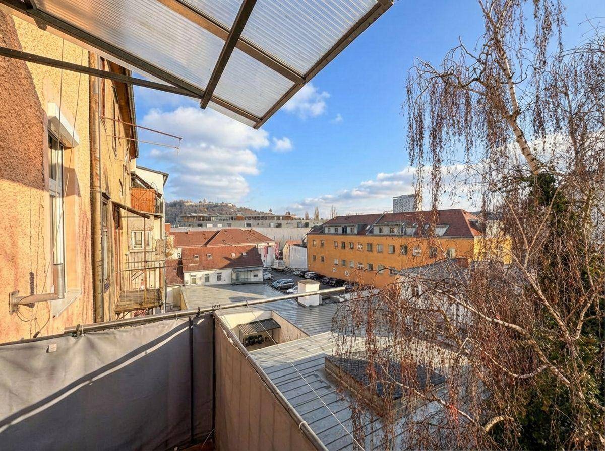 Balkon mit Blick auf die umliegenden Gebäude und eine grüne Hügellandschaft in der Ferne.