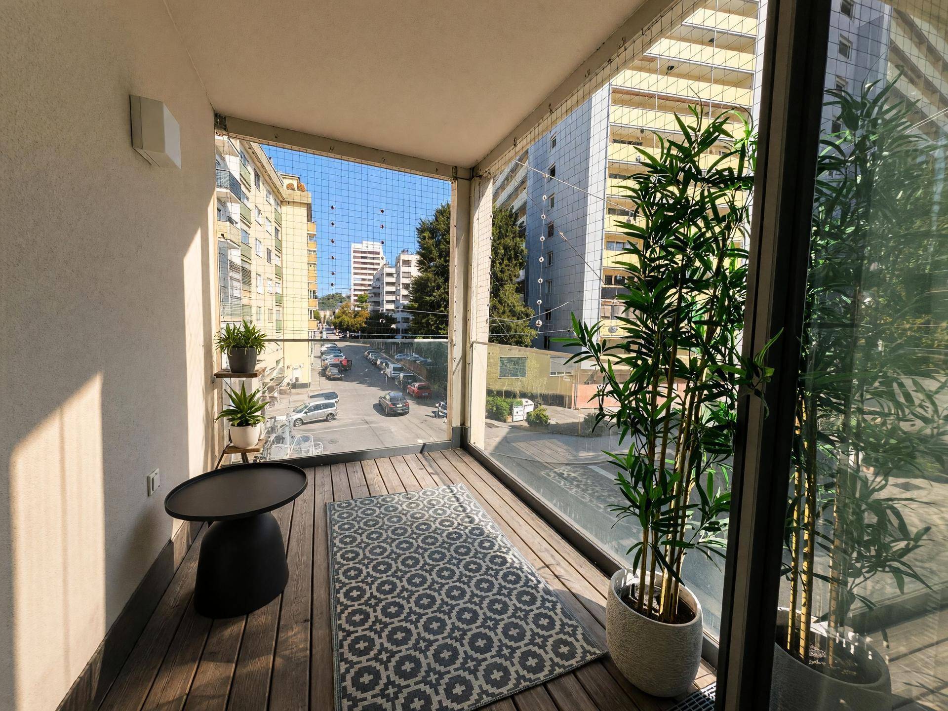 Sonniger Balkon mit Holzboden, Pflanzen und einem kleinen Tisch, bietet Stadtblick.