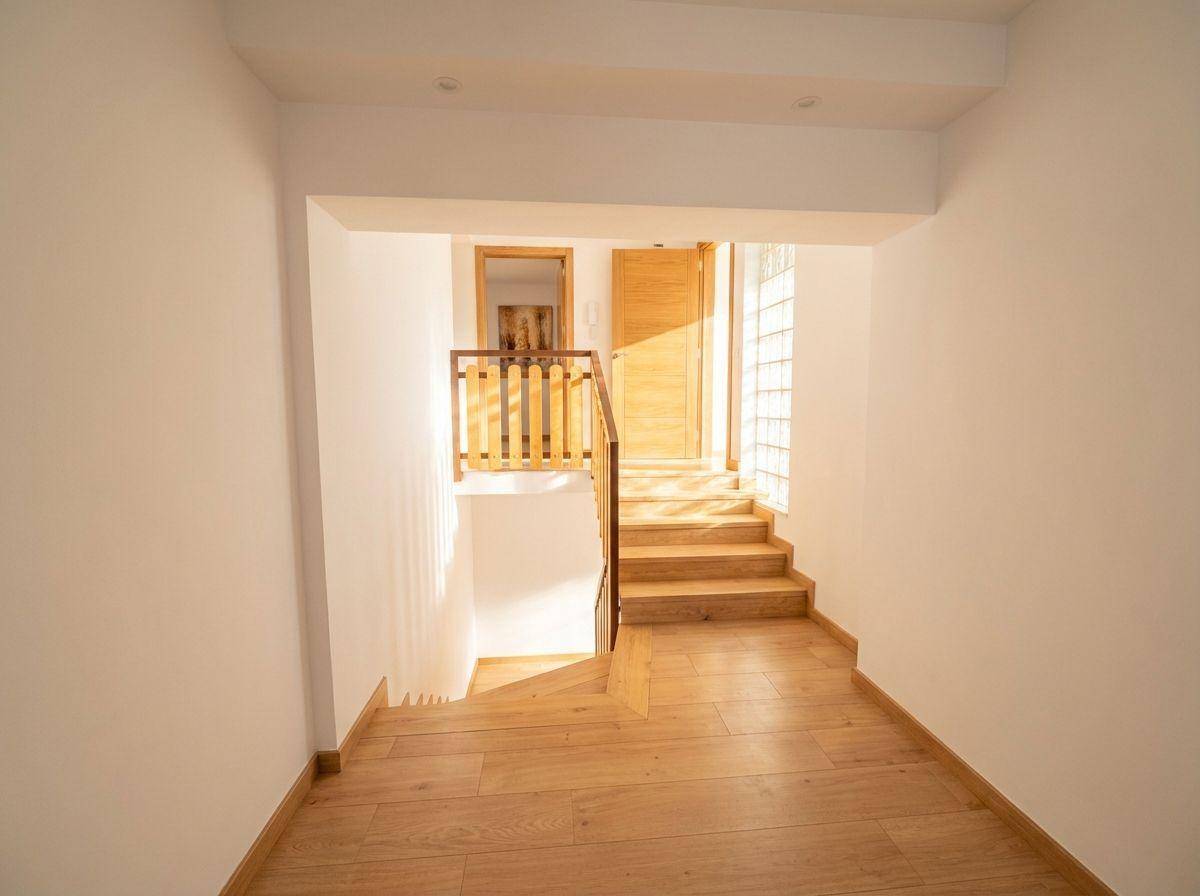 Eingangsbereich mit Holztreppe, Holzboden und einer Glasbausteinwand, die natürliches Licht hereinlässt.