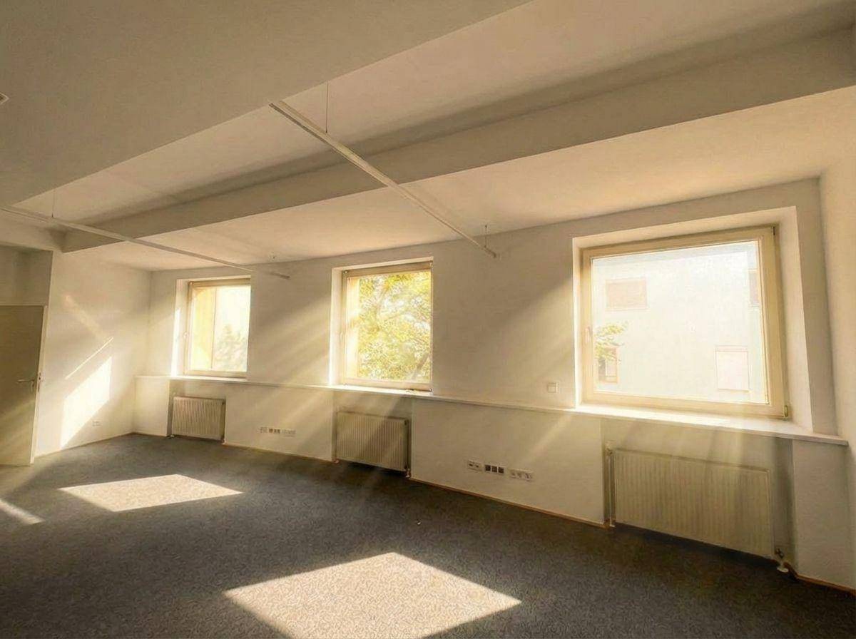 Blick auf die Fensterfront eines Büroraums mit Heizkörpern darunter und viel Sonnenlicht.