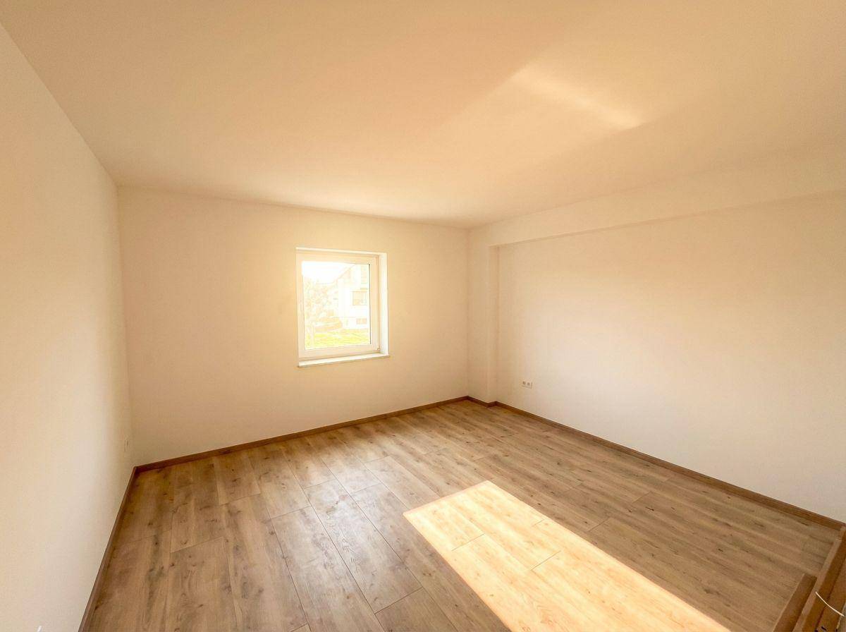Helles, leeres Zimmer mit Laminatboden und einem Fenster, das viel Sonnenlicht hereinlässt.