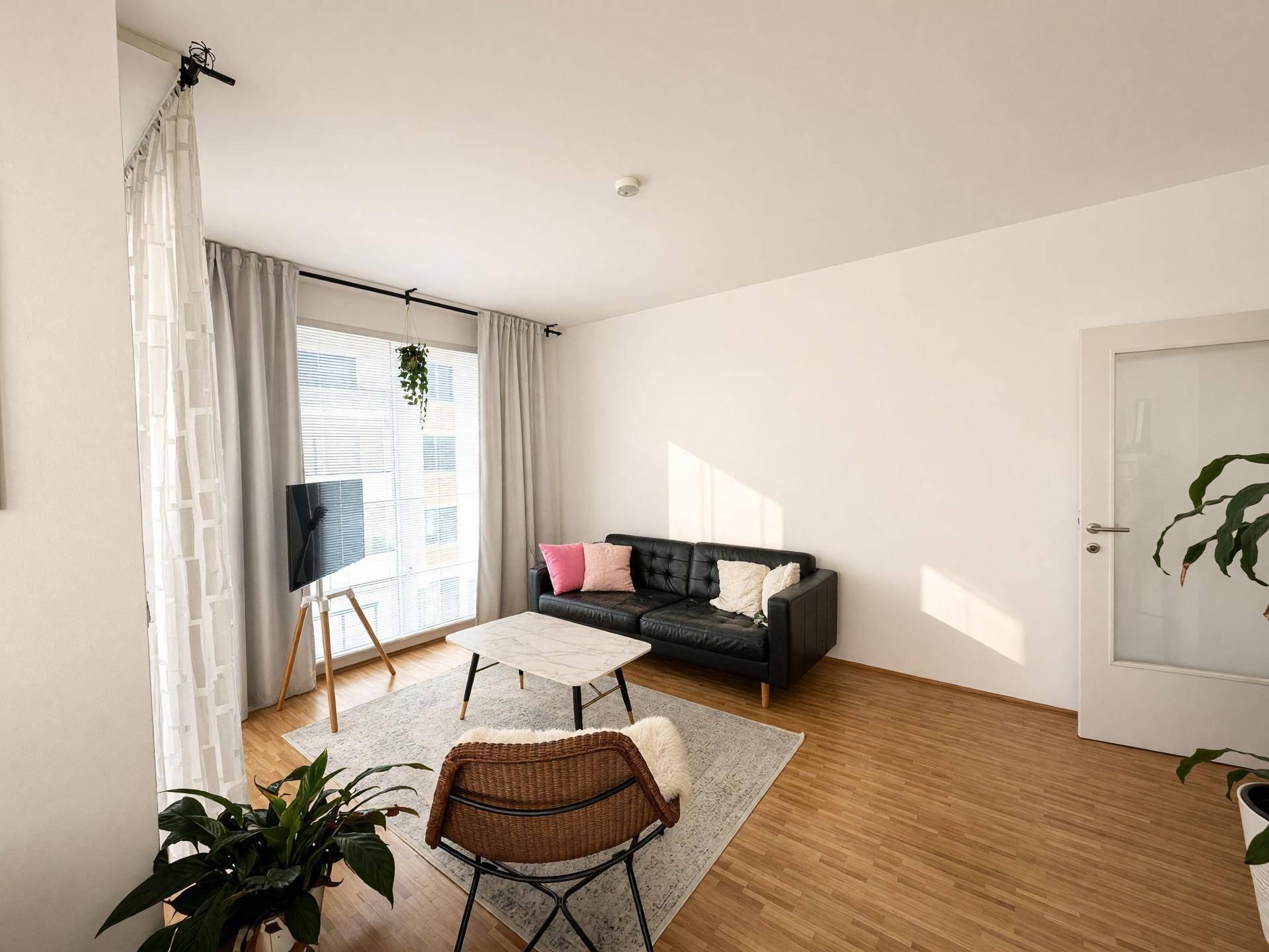 Wohnbereich mit schwarzem Sofa, Couchtisch und großem Fenster, das viel Licht spendet.