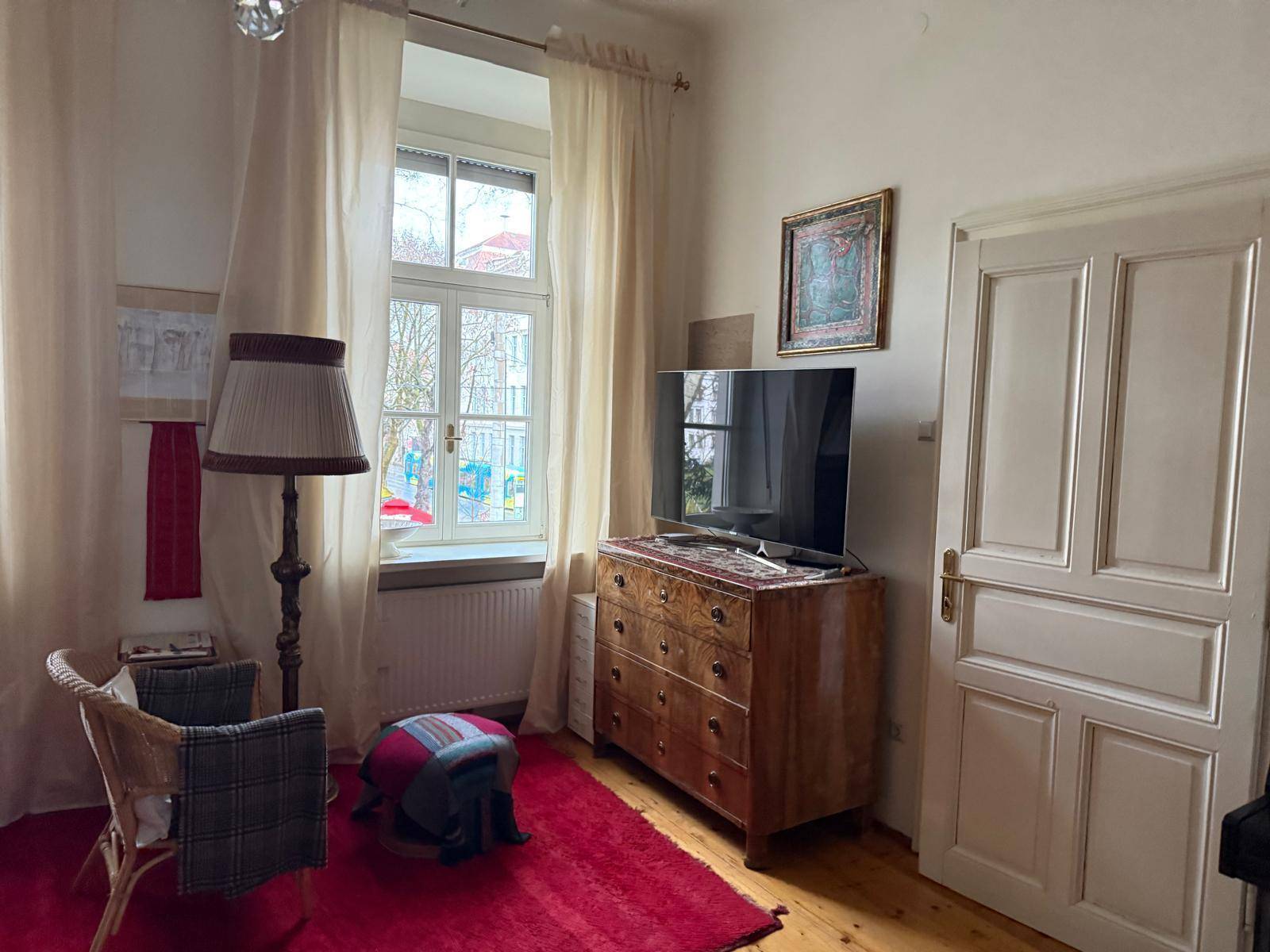 Gemütliches Wohnzimmer mit Holzboden, Fernseher auf Kommode und einem großen Fenster.
