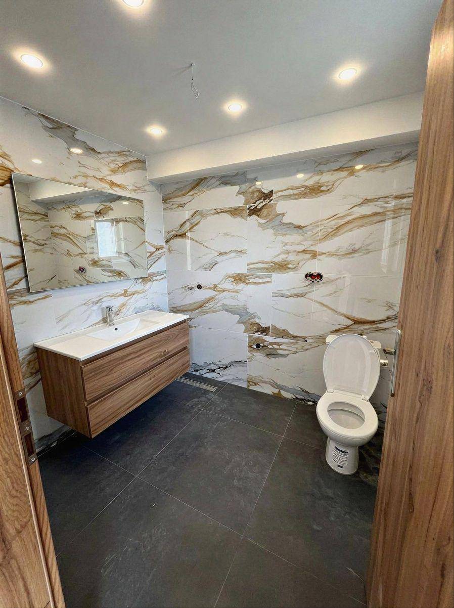 Elegantes Badezimmer mit großformatigen Marmorfliesen, schwebendem Waschtisch und dunklem Fliesenboden.