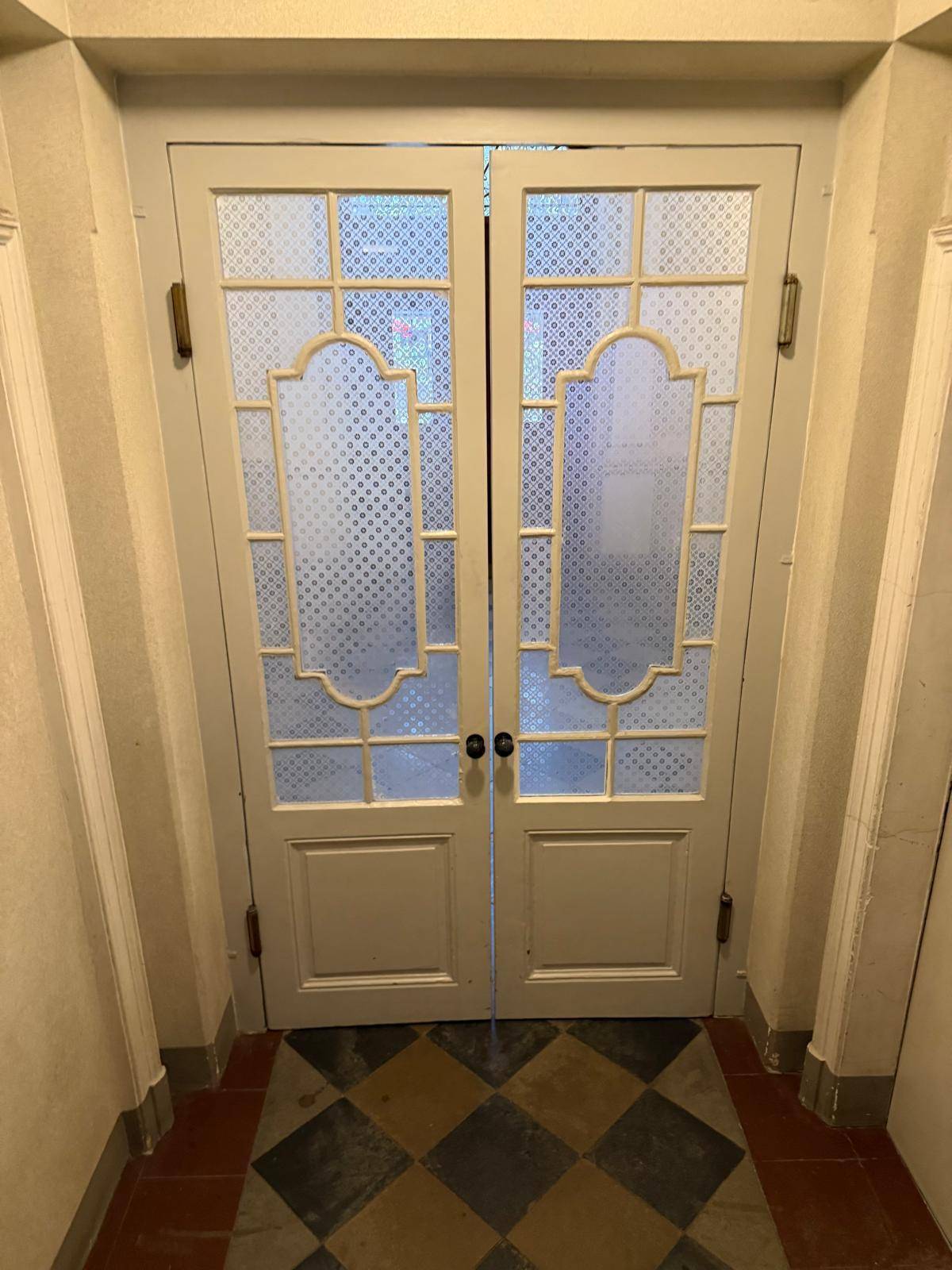Eingangsbereich mit gemusterten Glastüren und Schachbrettmuster-Boden in einem Altbau.