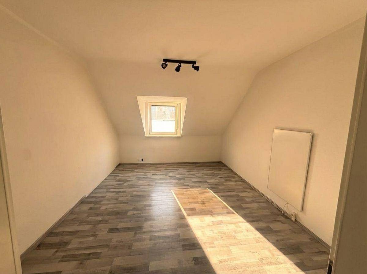 Leeres Zimmer im Dachgeschoss mit Laminatboden, schrägen Wänden und viel Tageslicht.