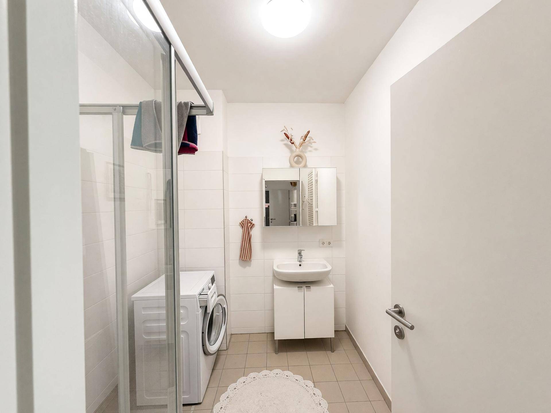 Modernes Badezimmer mit Dusche, Waschbecken und integrierter Waschmaschine.